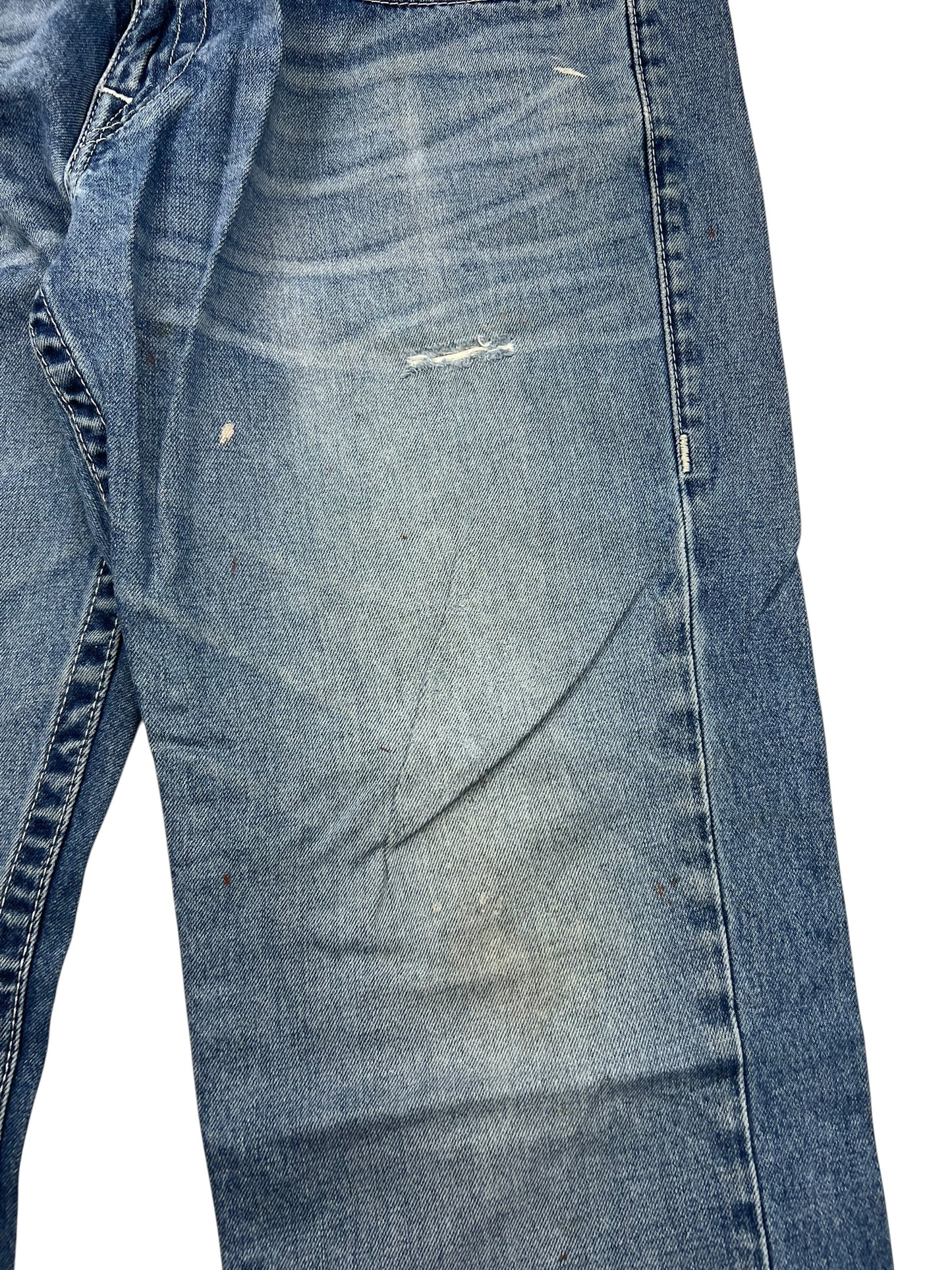 Ein Paar True Religion Straight Jeans in Größe 34 (L) von ZAZA resell, mit einem kleinen Riss, verblasste Bereiche, leichte Flecken auf dem Oberschenkel, und ein insgesamt gealtert, notleidenden Blick.