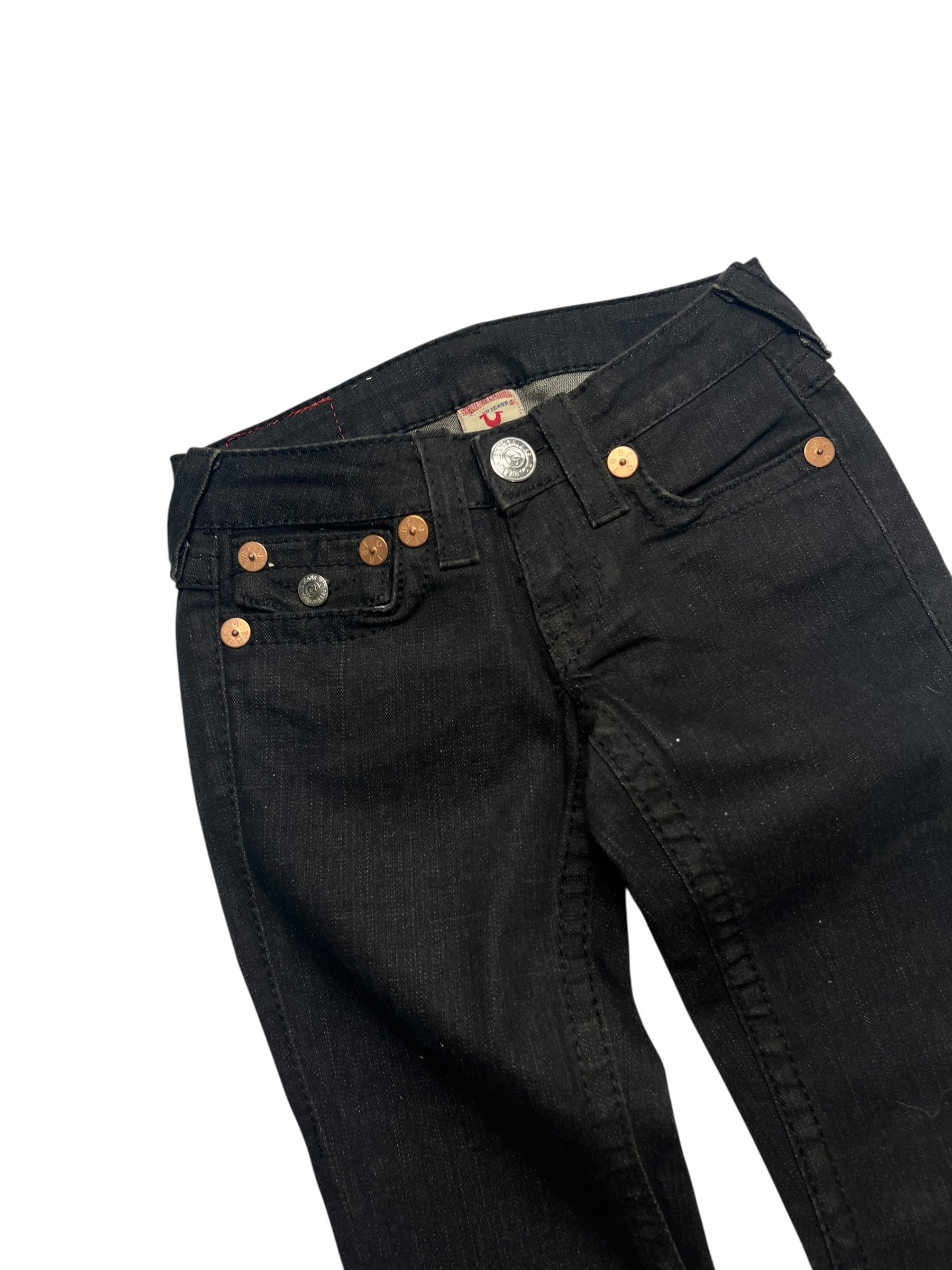Die True Religion Joey - Low Rise Boot Jeans in Größe 24 (XXS) von ZAZA resell, verfügen über schwarzen Denim mit metallischen Nieten, einen sichtbaren Knopfverschluss und eine verkürzte Außenbeinlänge, die flach auf einem weißen Hintergrund dargestellt wird.