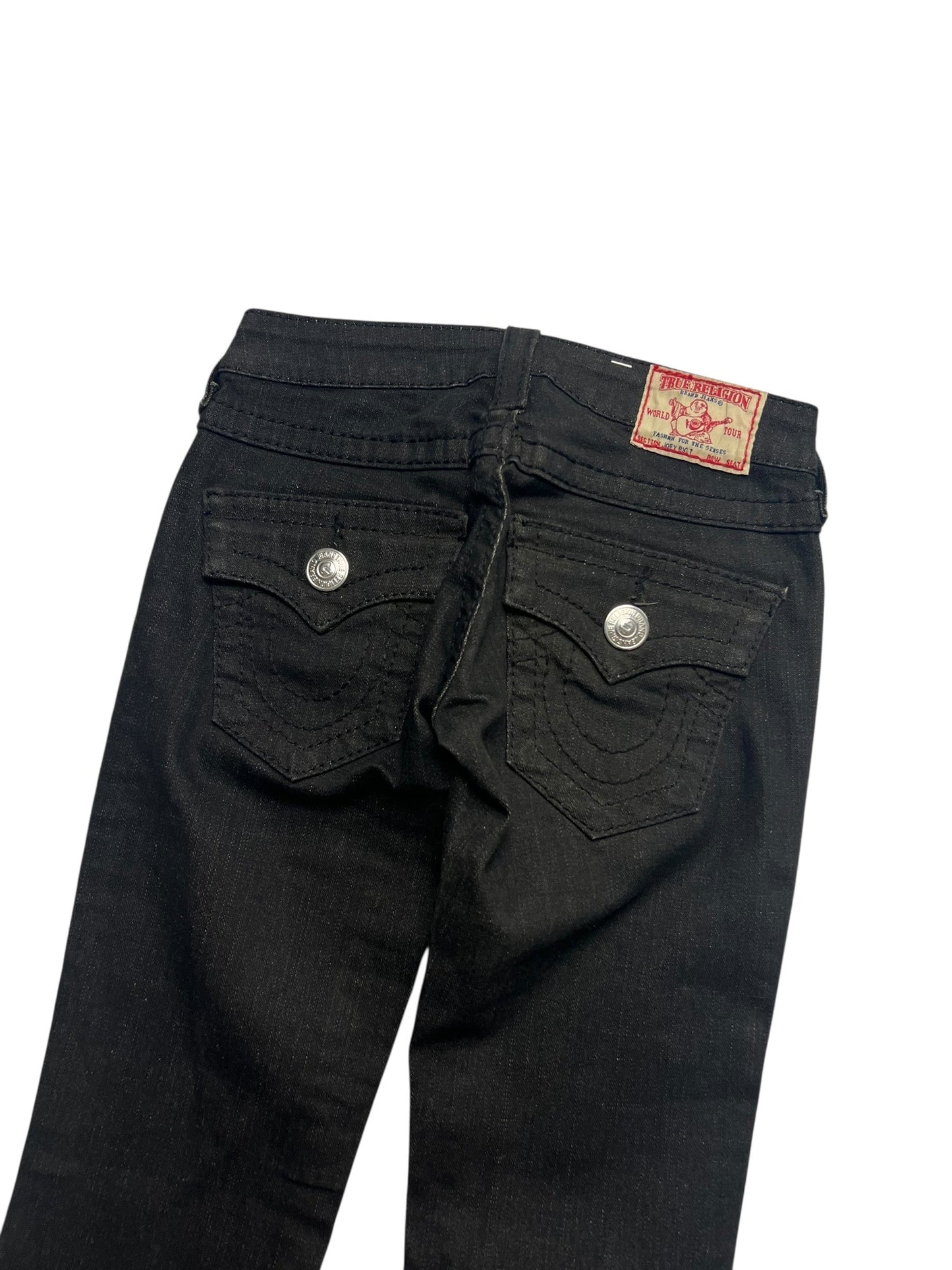 Die True Religion Joey - Low Rise Boot Jeans von ZAZA resell in Größe 24 (XXS) hat schwarzen Denim, zwei Pattentaschen hinten mit silbernen Knöpfen, ein rotes und hellbraunes Etikett am Bund und eine abgeschnittene Außennaht für einen modernen Look.