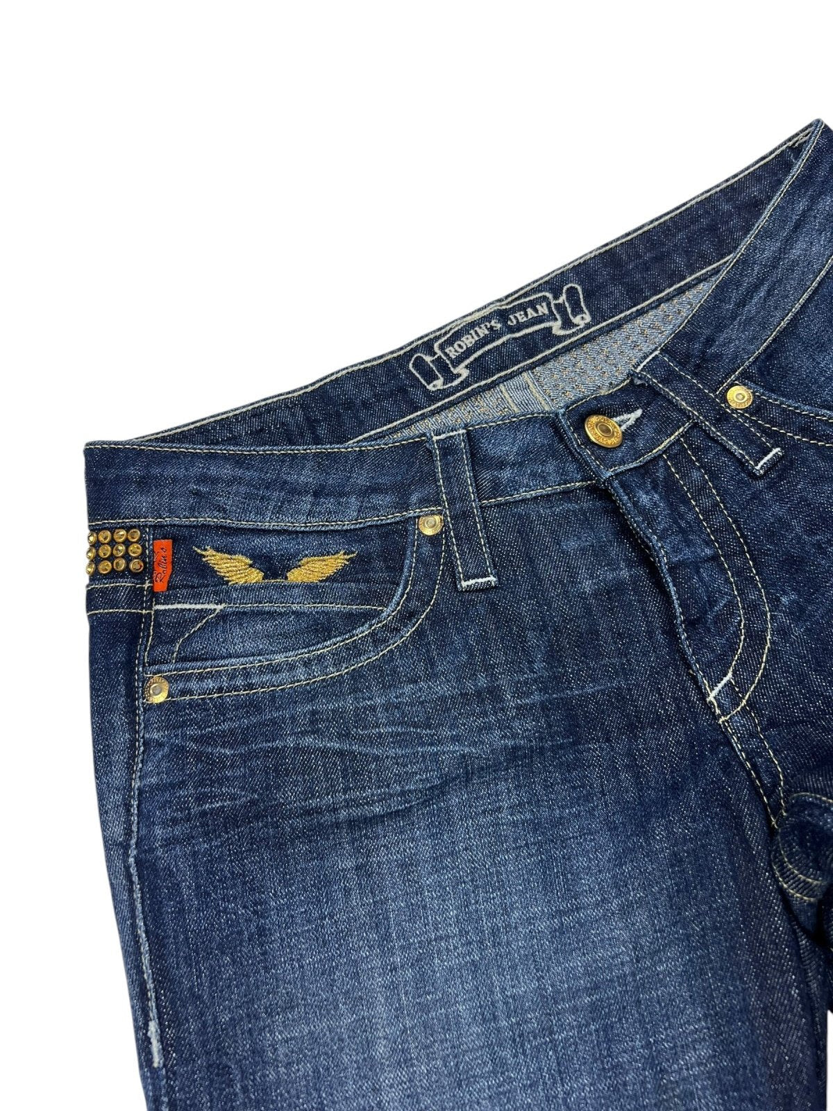 Robin's Jean Low Rise Boot | 26 (S) von ZAZA resell: Dunkelblaue Denim-Jeans mit goldenen Nähten, Messingnieten, rotem Taschenanhänger auf der Vorderseite, goldenem Flügeldesign in der Nähe der Tasche, metallischen Nieten am Bund; Bundweite und Labelgröße auf Ronnie Jeans Label.