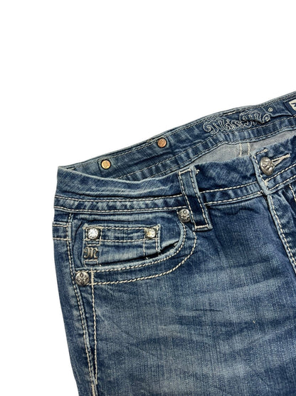 Nahaufnahme der Miss Me Mid Rise Boot Jeans von ZAZA resell in Größe 30 (M) aus blauem Denim mit weißen Nähten, Metallnieten, bestickten Taschen, einer kleinen Vordertasche, Gürtelschlaufen und einem gut lesbaren Größenetikett.