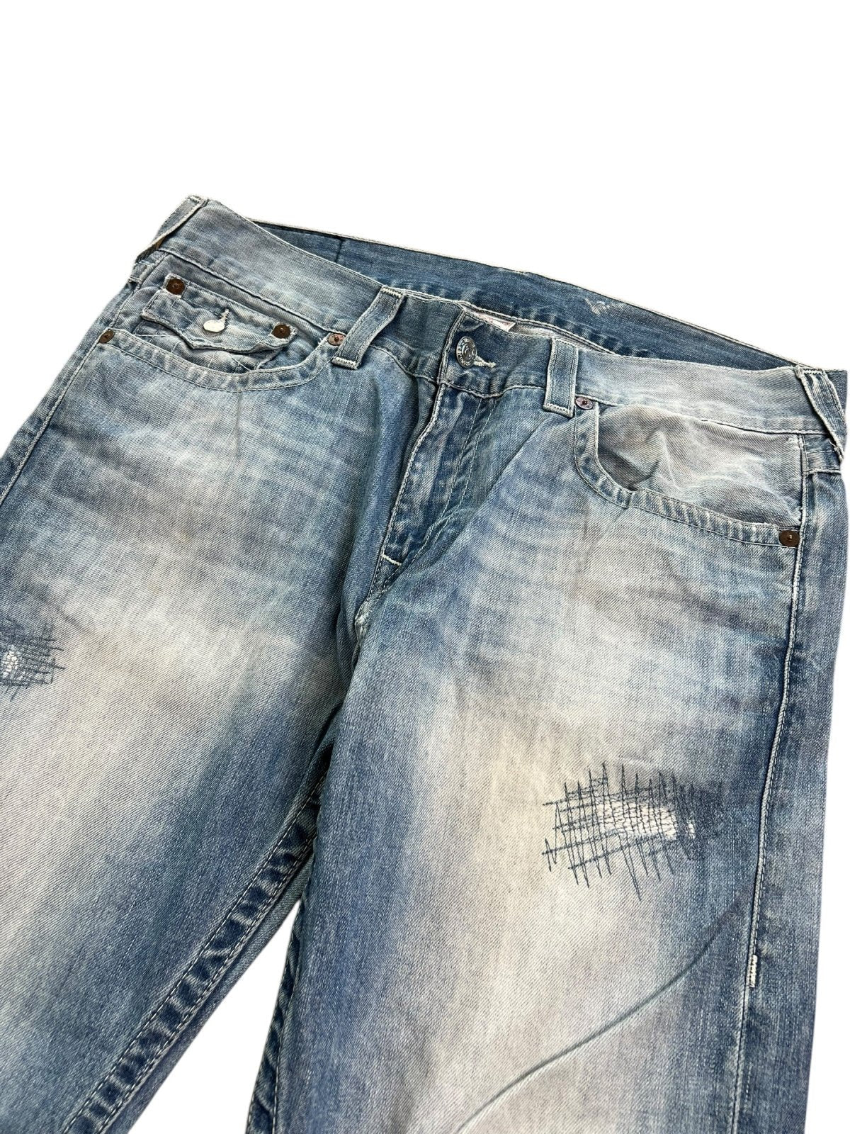 Die True Religion Straight Jeans von ZAZA resell in Größe 36 (XL) hat eine hellblaue Waschung, Distressed-Details, Patchwork-Nähte an den Oberschenkeln und eine Bundweite, die flach auf weißem Grund liegt.