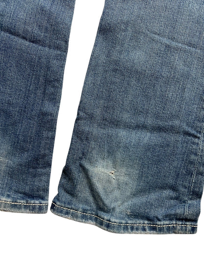 Die Nahaufnahme der Miss Me Low Rise Boot Jeans (Größe 26, S) von ZAZA resell zeigt verblichenen blauen Denim und einen kleinen Riss in der Nähe des Saums. Die Jeans liegt flach auf einem weißen Hintergrund. Labelgröße und Bundweite sind auf Anfrage erhältlich.