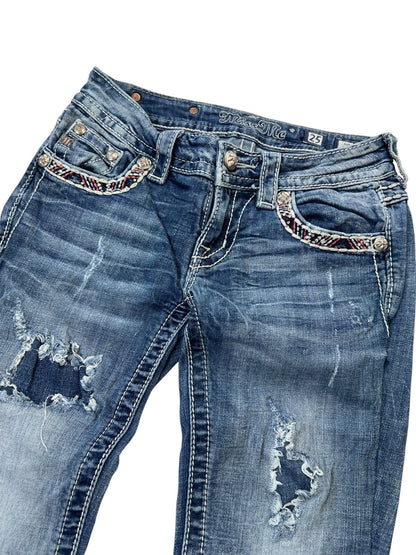 Die Miss Me Low Rise Straight Jeans von ZAZA resell in Größe 25 (XS/S) hat einen Used-Look mit blauem Distressed-Denim, ausgefransten Löchern an beiden Beinen, Nähten an den Vordertaschen und einer detaillierten Bundweite. Ausgestellt vor einem weißen Hintergrund.