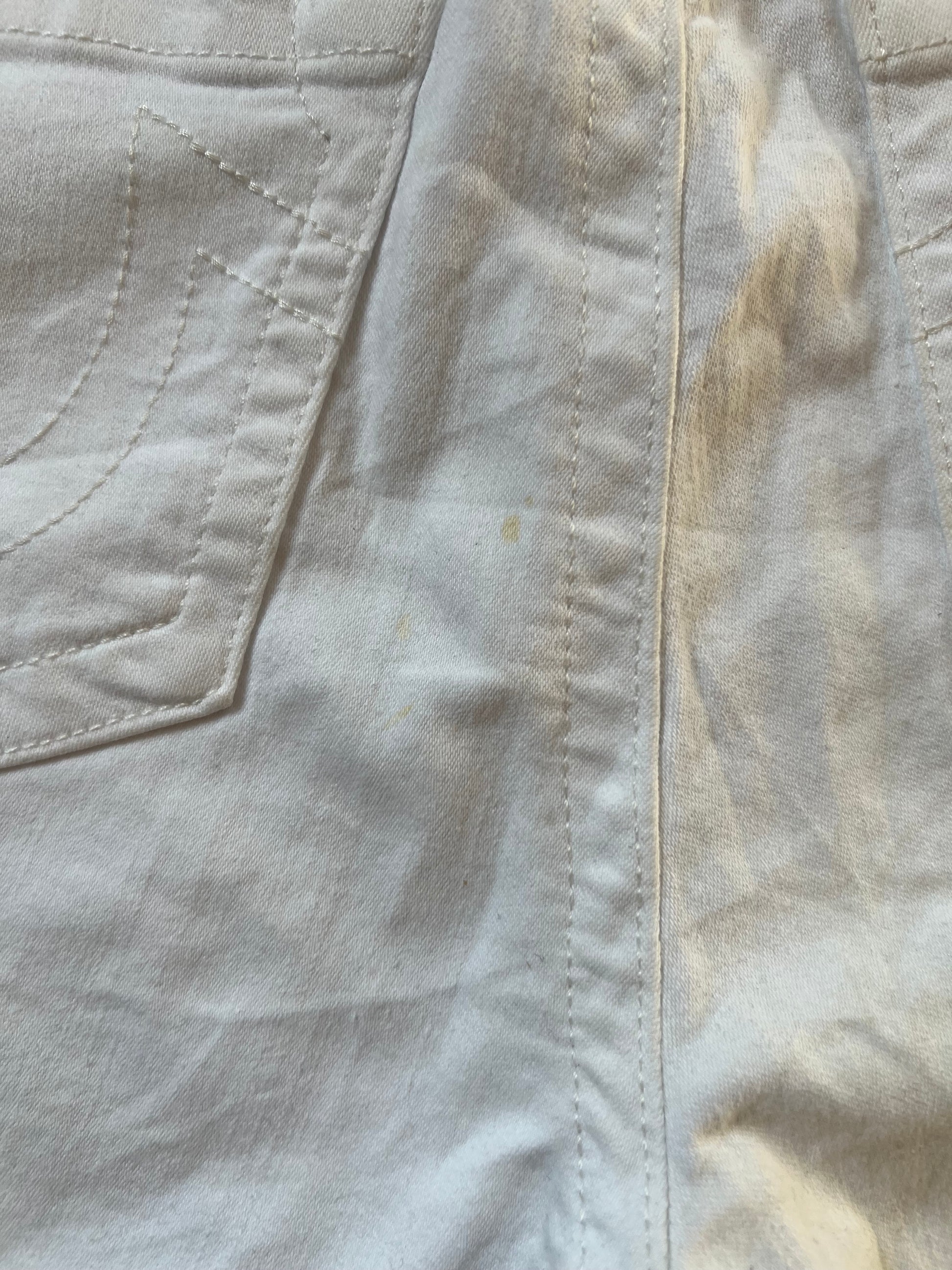 Nahaufnahme der weißen True Religion Mid Rise Shorts (Größe 30, Bundweite 39) von ZAZA resell, die eine linke Tasche und schwache gelbe Flecken in der Nähe der Mittelnaht zeigt. Der Stoff erscheint leicht zerknittert.
