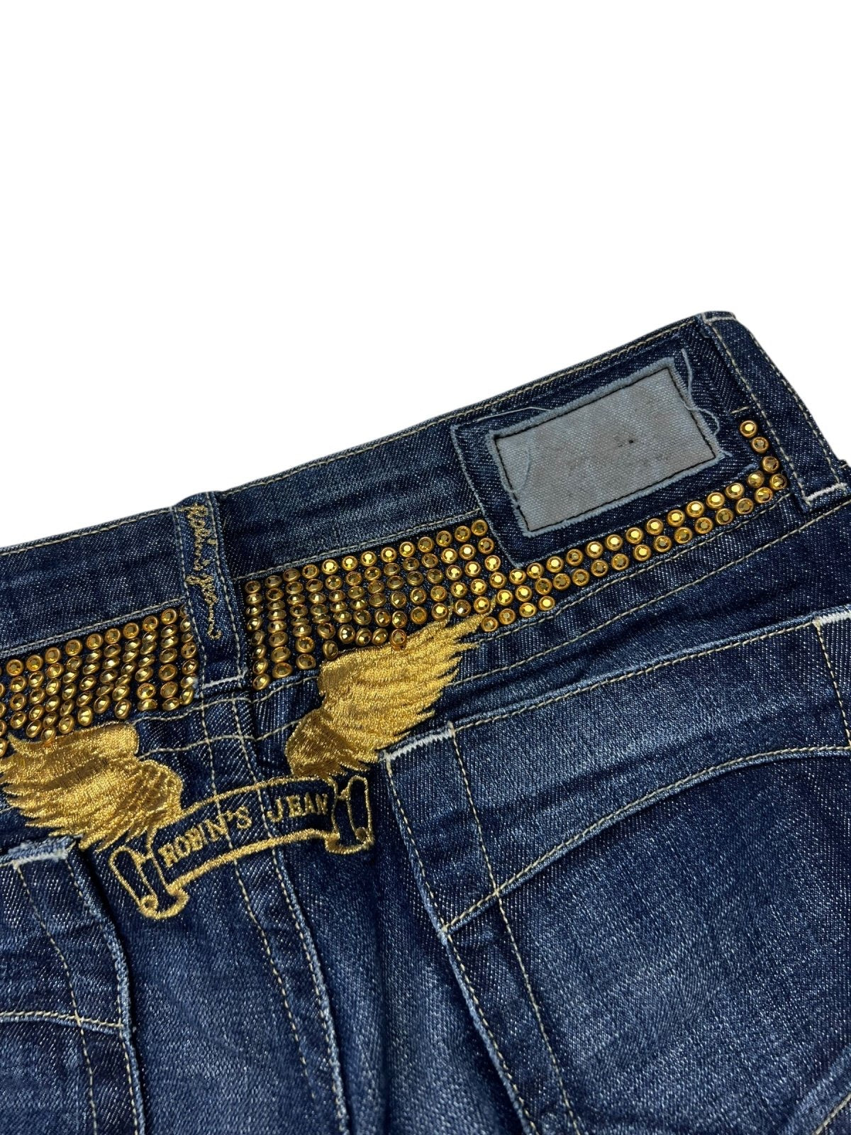 Eine Nahaufnahme des Robin's Jean Low Rise Boot von ZAZA resell in Größe 26 (S) zeigt goldene Nieten- und Flügelstickereien, ein Robins-Jean-Logo über den Gesäßtaschen und einen verblichenen Aufnäher am Bund mit Größenangaben.