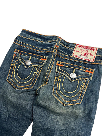 Eine Nahaufnahme der True Religion Billy Super T Jeans von ZAZA resell in Größe 27 (M) zeigt blauen Denim, gelb-orangefarbene Nähte, zwei detaillierte Gesäßtaschen, silberne Knöpfe und ein rot-weißes Label, das Bundweite und gekürzte Außenbeinlänge hervorhebt.