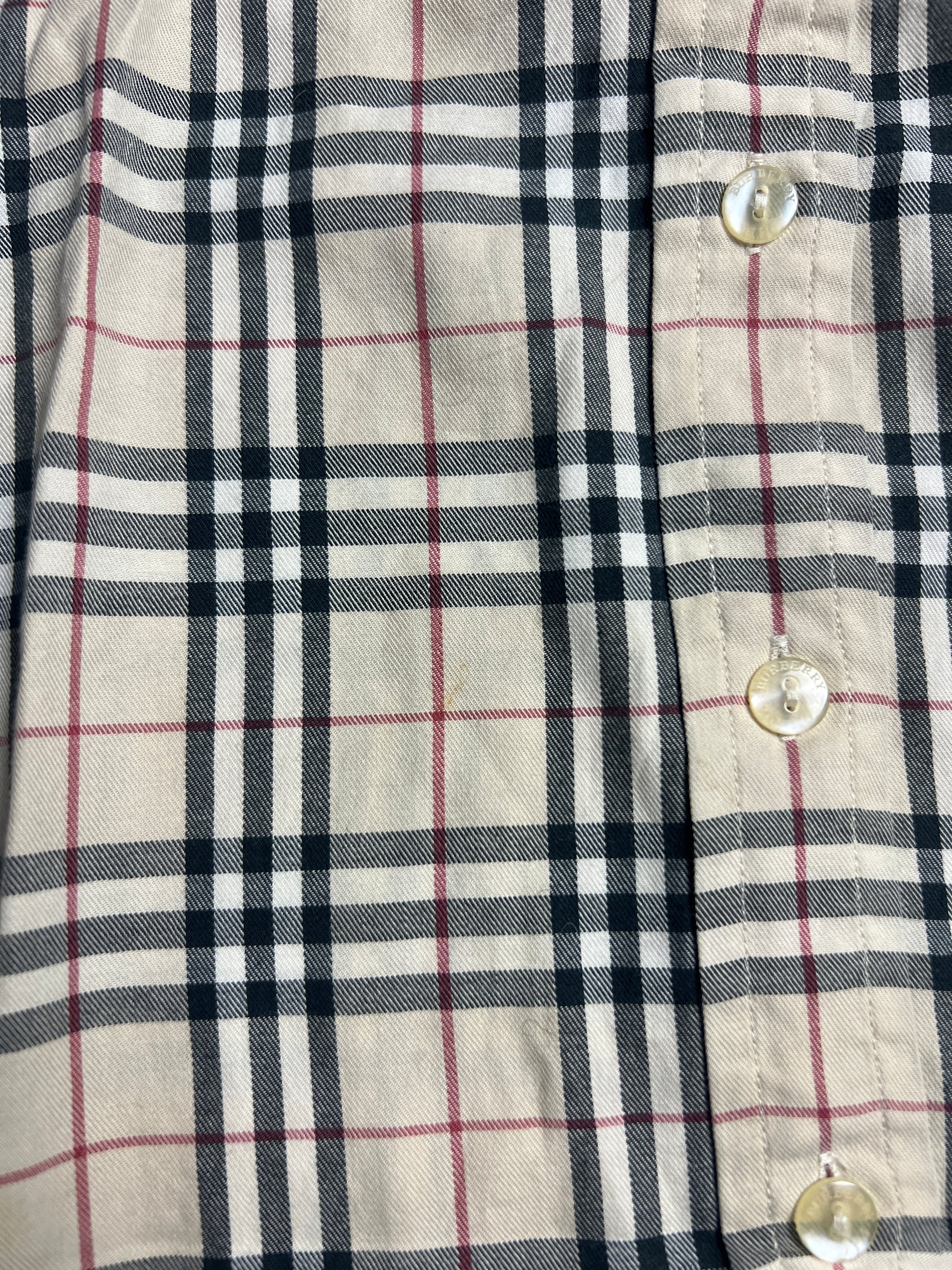 Nahaufnahme eines beigen Burberry Hemd | S aus dem ZAZA-Wiederverkauf, mit einem schwarz-weiß-roten Karomuster und drei durchsichtigen Knöpfen auf der rechten Seite. Zustand 9/10. Maße in cm und Labelgröße S auf Anfrage erhältlich.