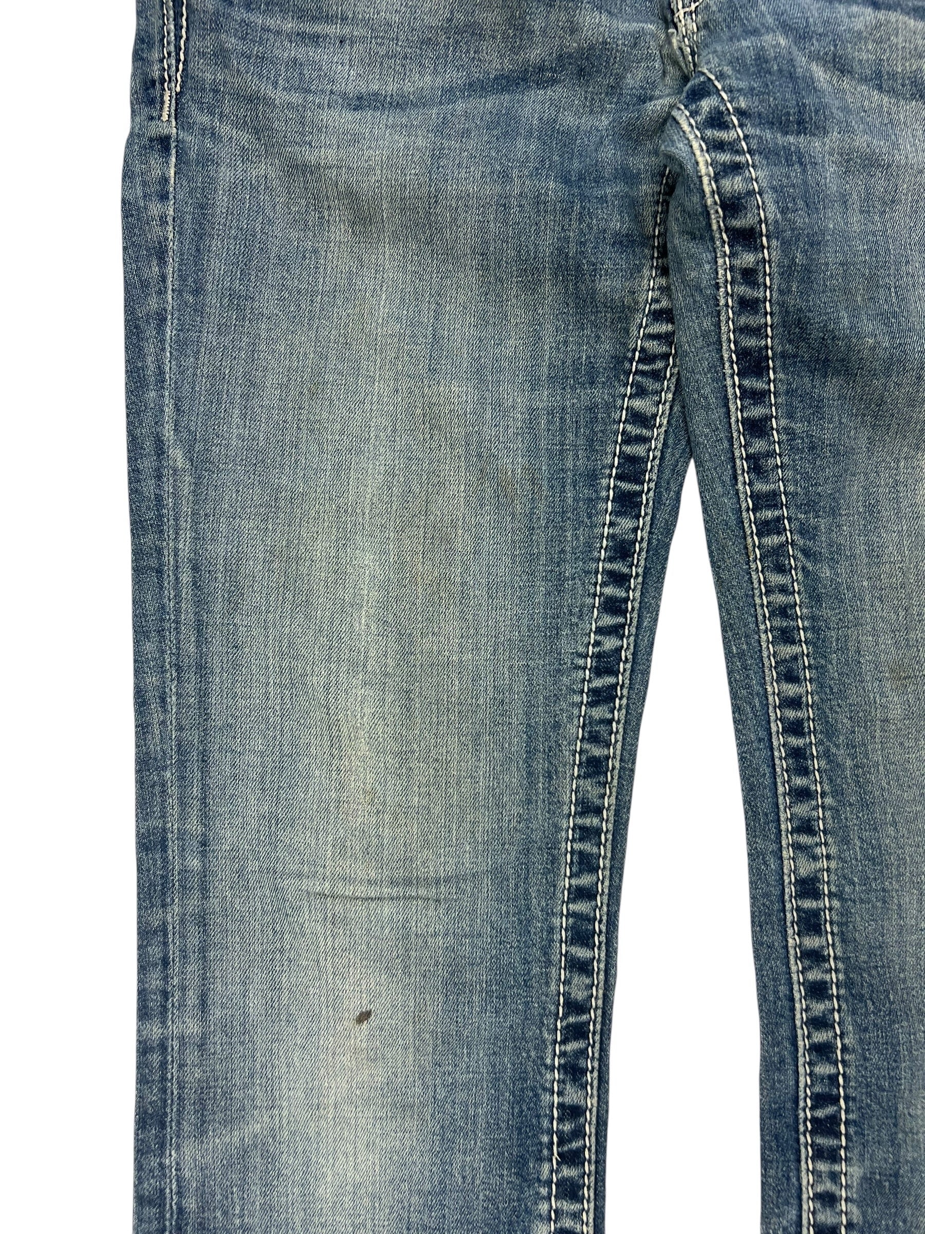 Eine Nahaufnahme der Miss Me Low Rise Straight Jeans von ZAZA resell, Größe 27 (S), aus blauem Denim mit abgenutztem, verblichenem Stoff, sichtbaren Nähten und einem kleinen dunklen Fleck in der Nähe des Knies.