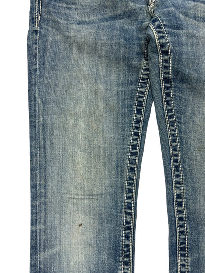 Eine Nahaufnahme der Miss Me Low Rise Straight Jeans von ZAZA resell, Größe 27 (S), aus blauem Denim mit abgenutztem, verblichenem Stoff, sichtbaren Nähten und einem kleinen dunklen Fleck in der Nähe des Knies.