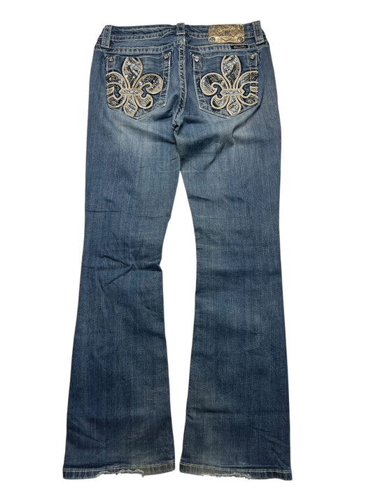 Die ZAZA resell Miss Me Mid Rise Boot in Größe 30 (M) präsentiert eine blaue Bootcut-Jeans mit großer Fleur-de-Lis-Stickerei auf den Gesäßtaschen, einem Marken-Lederpatch und detaillierten Bundweitenmaßen für einen perfekten Sitz.