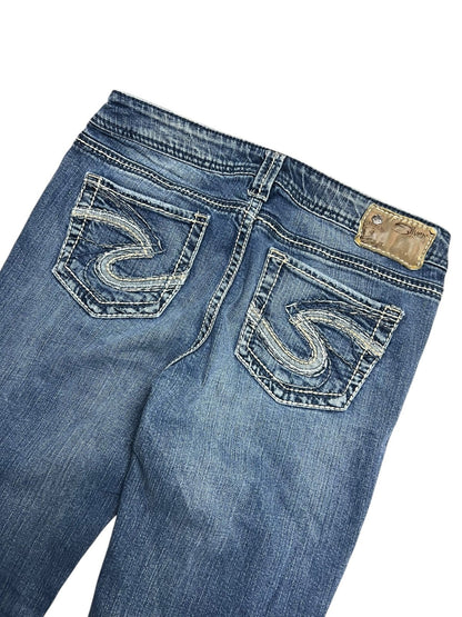 Die Silver Jeans Low Rise Boot von ZAZA resell in Größe 29 (M) ist eine blaue Jeans in Rückenansicht mit zwei weiß bestickten Gesäßtaschen, einem hellbraunen Lederbundaufnäher und einem Etikett mit Bundweite und Labelgröße.