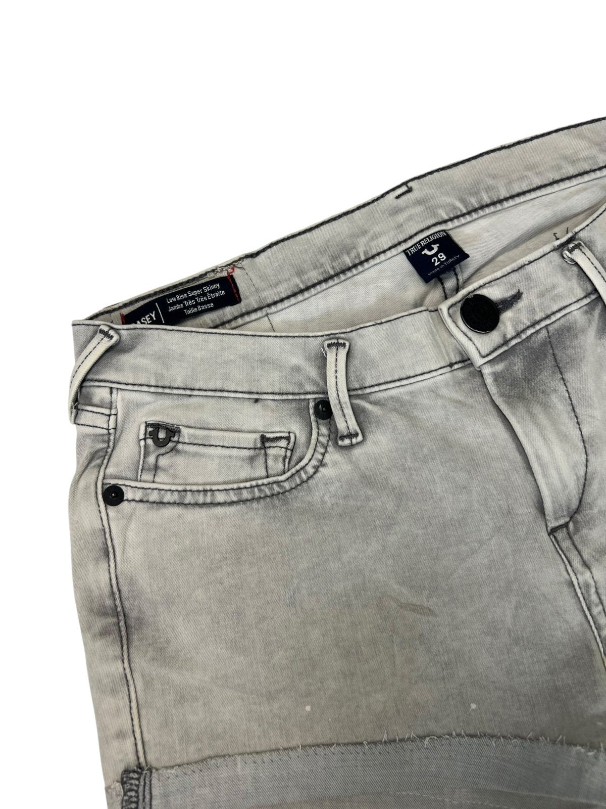 Eine Nahaufnahme der True Religion Shorts aus hellgrauem Denim mit verblasstem Distressed-Look von ZAZA resell. Zur Ausstattung gehören Bund, Vordertaschen, Gürtelschlaufen und ein Größenetikett mit der Angabe 29 (M).