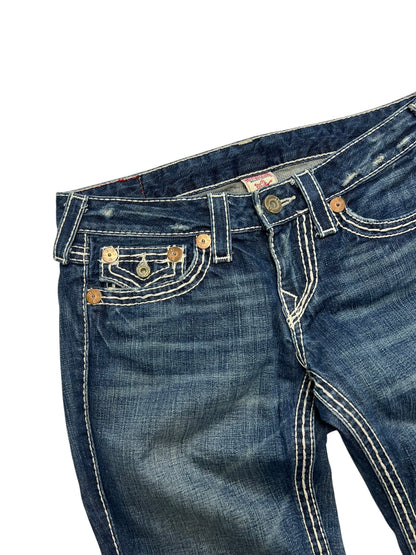 Eine Nahaufnahme der True Religion Joey Big T - Low Rise Boot Jeans (28/M) aus dem ZAZA-Wiederverkauf. Sie zeigt blauen Denim mit auffälligen weißen Nähten, Metallnieten an mehreren Taschen, einen leicht ausgeblichenen Look, Bundweite 40 markiert und den oberen vorderen Bereich teilweise gefaltet.