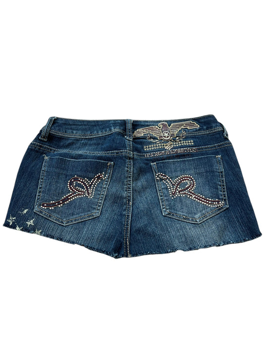 Der Rocawear Rock | W27 von ZAZA Resell besticht durch einen blauen Denim-Look mit Strass-Akzenten auf der Rückseite, einem dekorativen Detail über der rechten Tasche, dezentem Used-Look auf der linken Seite und Bundweite für einen bequemen Sitz. Perfekt für einen auffälligen Rock-Style.