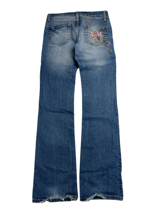 Die von ZAZA weiterverkauften Y2K Low Rise Boot Jeans (W26 x L30) sind blau, ausgestellt mit verblassten Details und einer mit Blumen bestickten Gesäßtasche, einem klassischen Hosenbund und einem weiten Beinausschnitt, flach auf weißem Hintergrund dargestellt.