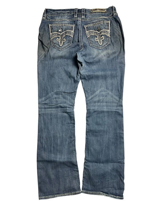 Die Rock Revival Mid Rise Boot Jeans von ZAZA resell, Größe 32 (XL), verfügt über dekorative Nähte an den Gesäßtaschen, eine leicht verblasste blaue Waschung und Bundweite 46 für eine bequeme Passform, hier von hinten.
