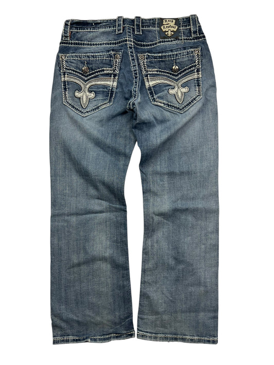 Die Rock Revival Relaxed Straight/Baggy Jeans von ZAZA resell in Größe 34 (M) sind aus blauem Denim, von hinten gesehen, mit Ziernähten und Stickereien auf beiden Gesäßtaschen sowie leichtem Fading auf dem Stoff.