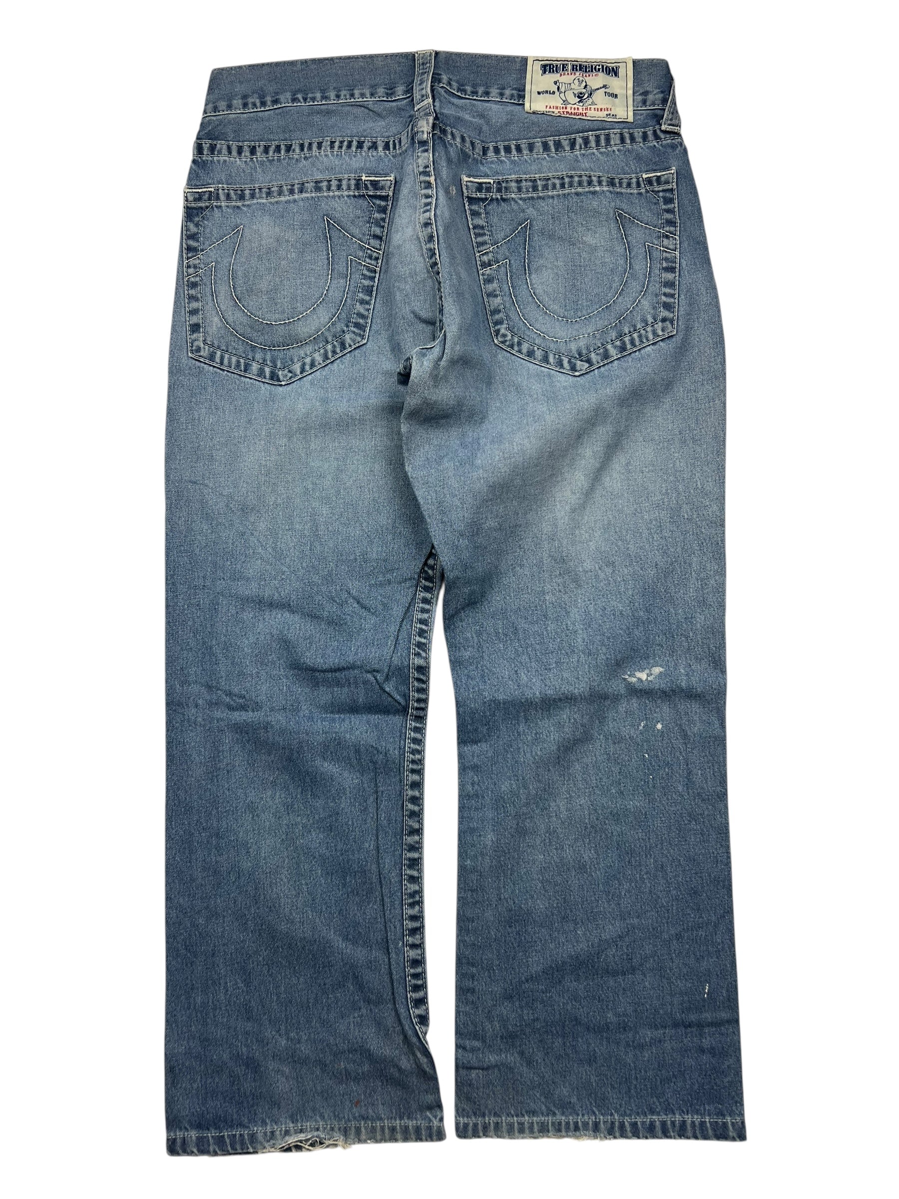 Ein Paar True Religion Straight-Jeans (Größe 34 L) von ZAZA resell, abgebildet von hinten mit zwei bestickten Hufeisentaschen, einem Markenaufnäher am Bund, einem leicht abgenutzten Look und Angaben zu Bundweite und Außenbeinlänge.