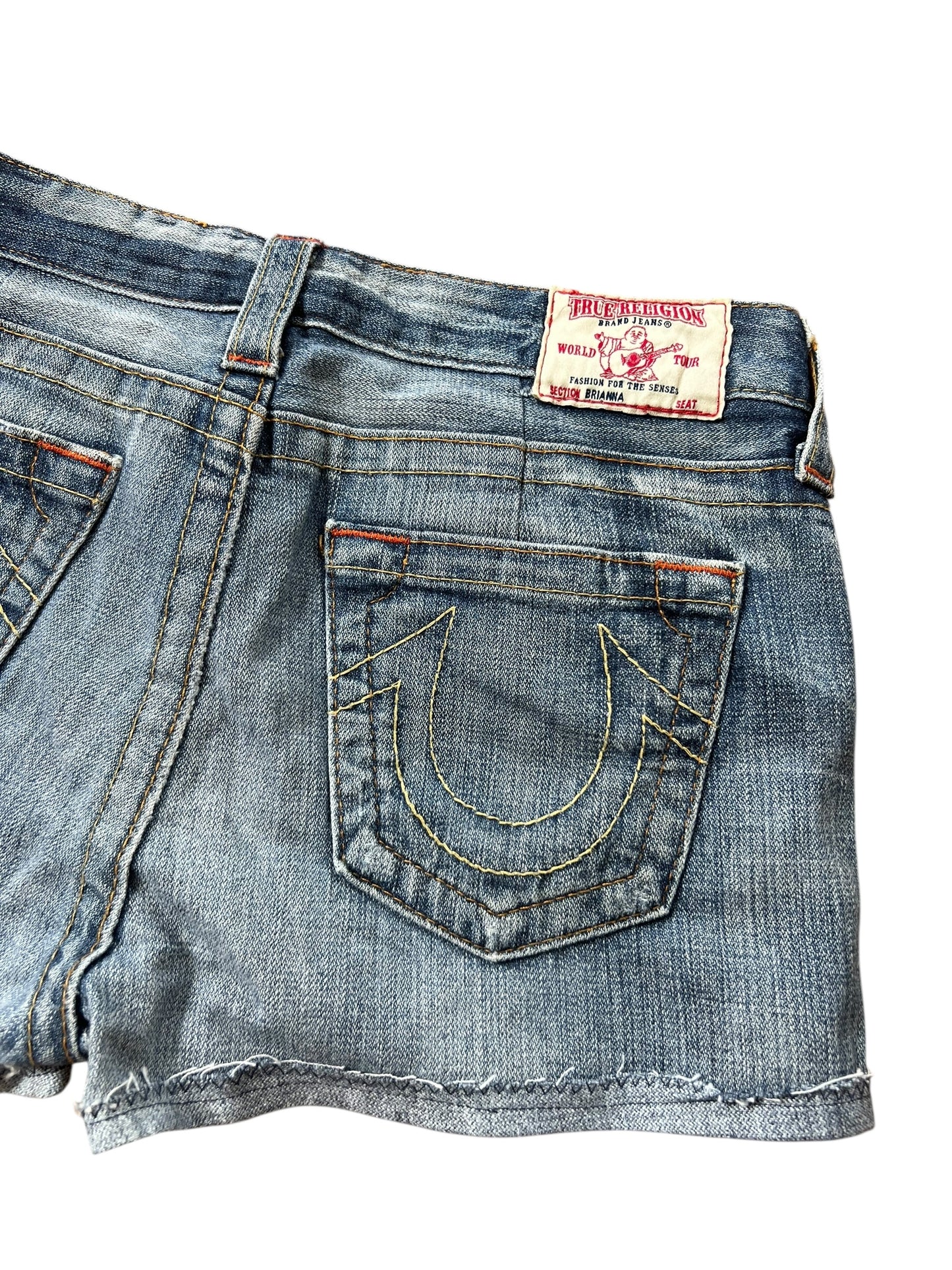 Eine Nahaufnahme der True Religion Shorts | 27 (M) von ZAZA resell aus blauem Denim, mit einer Gesäßtasche mit gelben Hufeisen-Nähten, einem True Religion-Label am Bund, Bundweite 39 und Labelgröße 27.