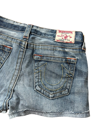 Eine Nahaufnahme der True Religion Shorts | 27 (M) von ZAZA resell aus blauem Denim, mit einer Gesäßtasche mit gelben Hufeisen-Nähten, einem True Religion-Label am Bund, Bundweite 39 und Labelgröße 27.