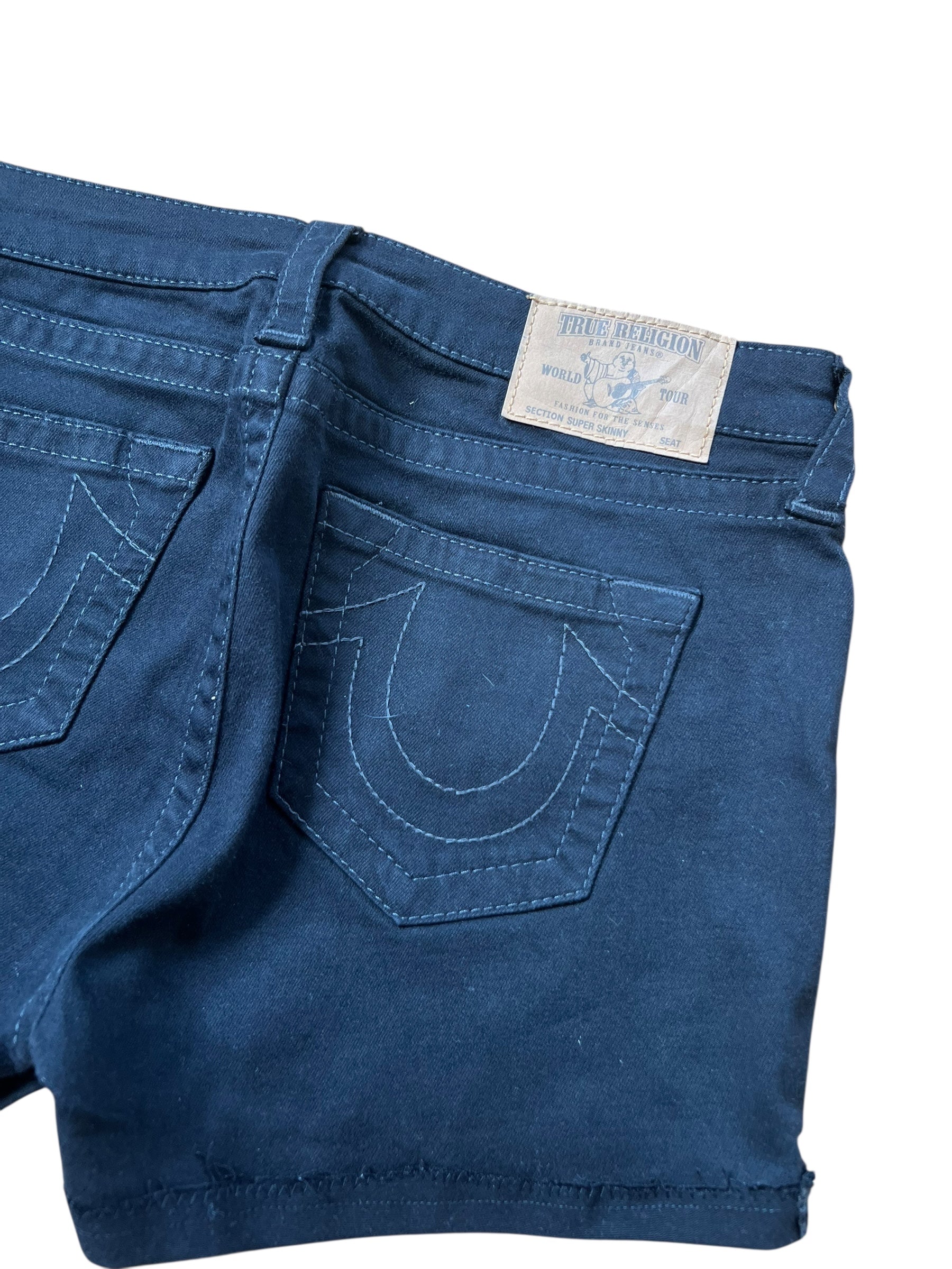 Eine Nahaufnahme der dunkelblauen True Religion Shorts (Größe 29/S) aus dem ZAZA-Wiederverkauf, die Gesäßtaschen mit weißen Nähten und ein Markenetikett am Bund zeigt.