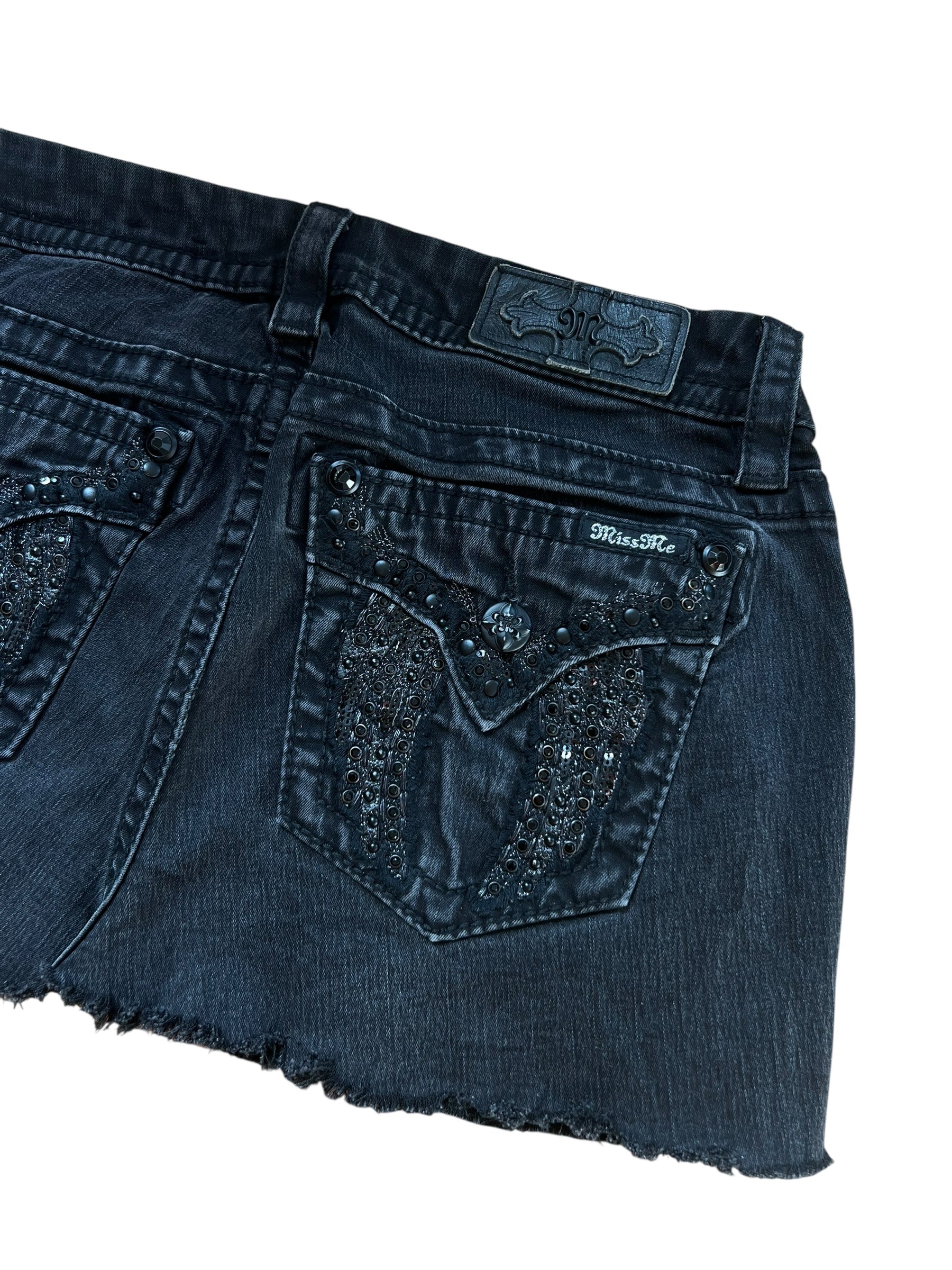 Miss Me Rock von ZAZA resell in Größe 29 (M), mit schwarzem Denim, rohem Saum, Ziernähten, Strasssteinen und einer Pattentasche hinten. Etikett und Größe sind oberhalb der Tasche sichtbar. Flach gelegt, Taille misst 39 cm auf weißem Hintergrund.