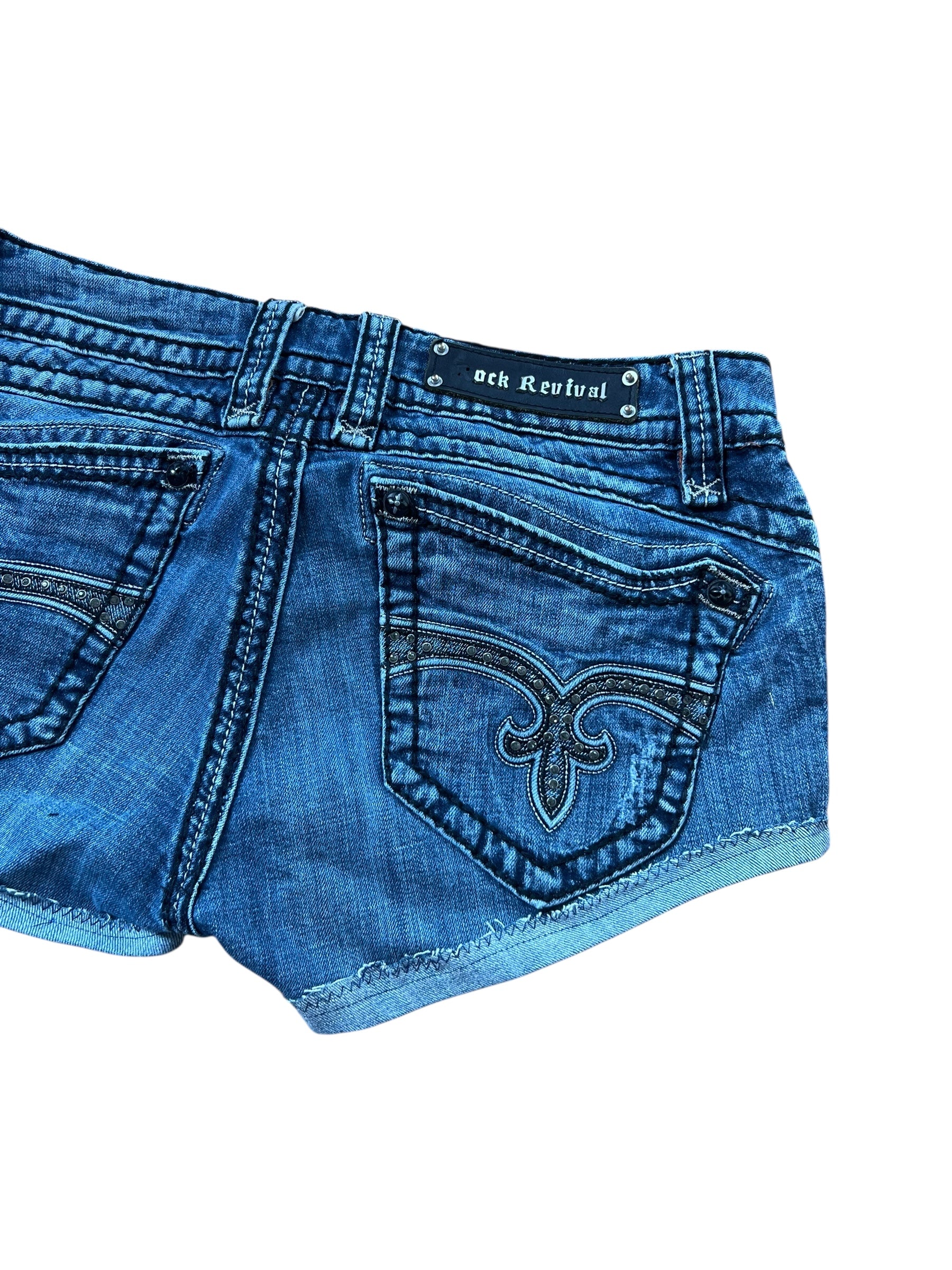Rock Revival Shorts | 31 (M) von ZAZA resell: blauer Denim mit dekorativen Nähten an den Gesäßtaschen, ausgefransten Säumen und einem schwarzen Rock Revival-Label. Die Shorts in Größe 31 sind teilweise auf weißem Hintergrund abgebildet.