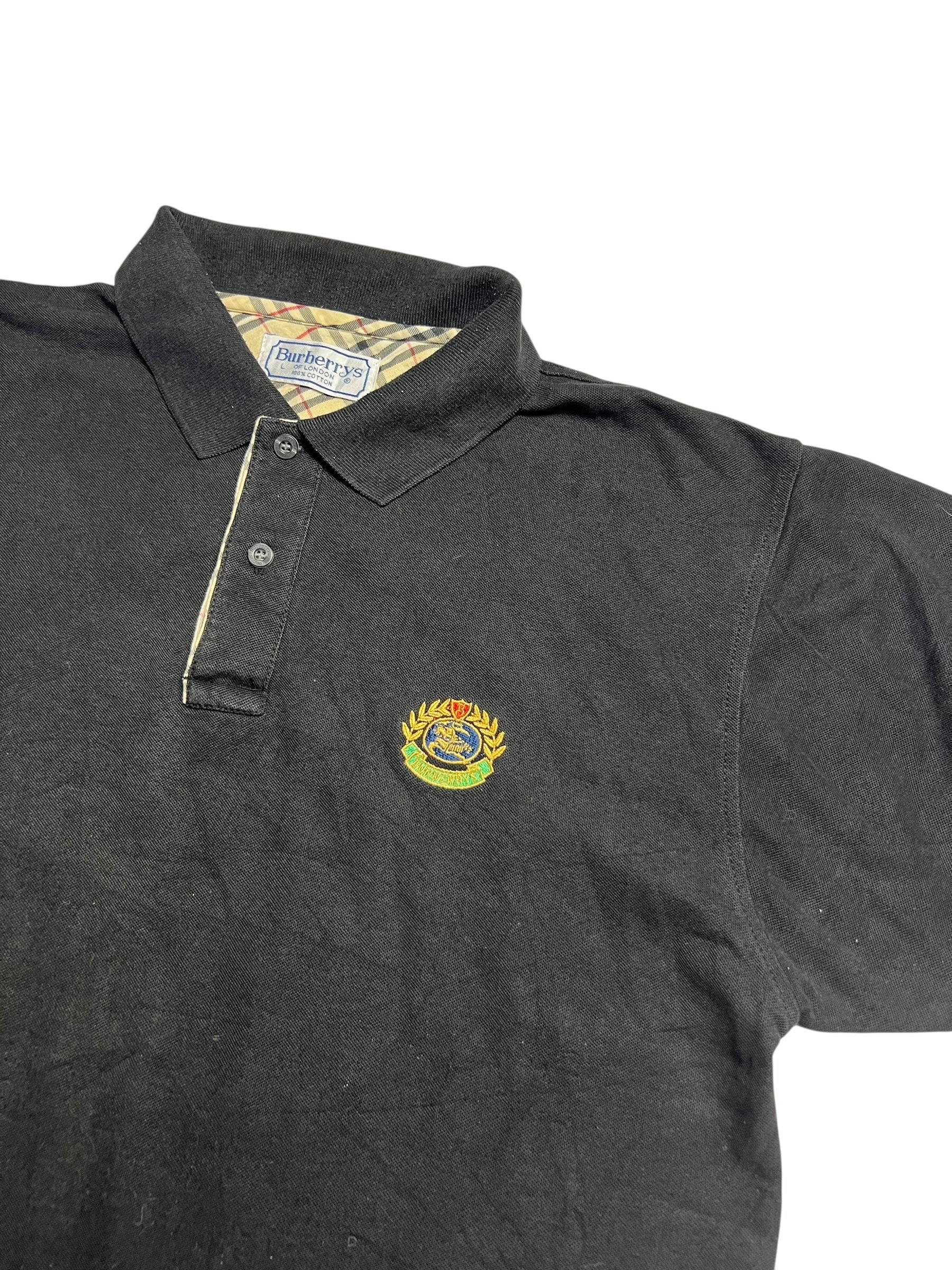 Burberry Polo Shirt | L von ZAZA resell: schwarz mit Kragen, Knopfleiste, gesticktem Wappenlogo auf der Brust, karierter Kragen mit Burberrys Label. Zustand 9/10. Labelgröße L. Maße in cm auf Anfrage.