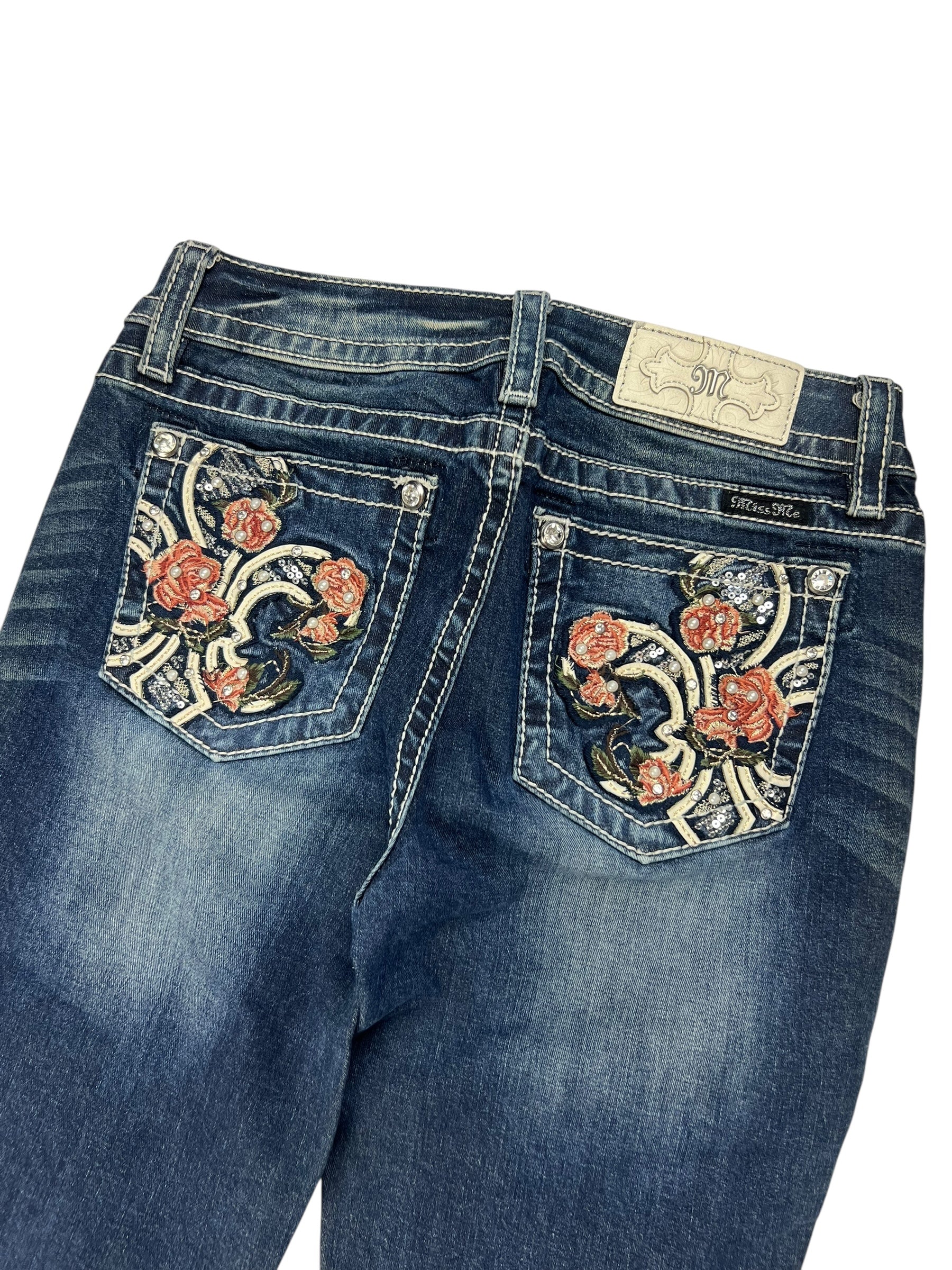 Die Miss Me Low Rise Boot Jeans von ZAZA resell in Größe 27 (S) hat blauen Denim mit ausgeblichenen Details, eine rote und rosa Blumenstickerei auf den Gesäßtaschen, ein weißes Markenpatch aus Leder am Bund und eine Passform, die als Außenbeinlänge und Bundweite für Größe 27 angegeben ist.