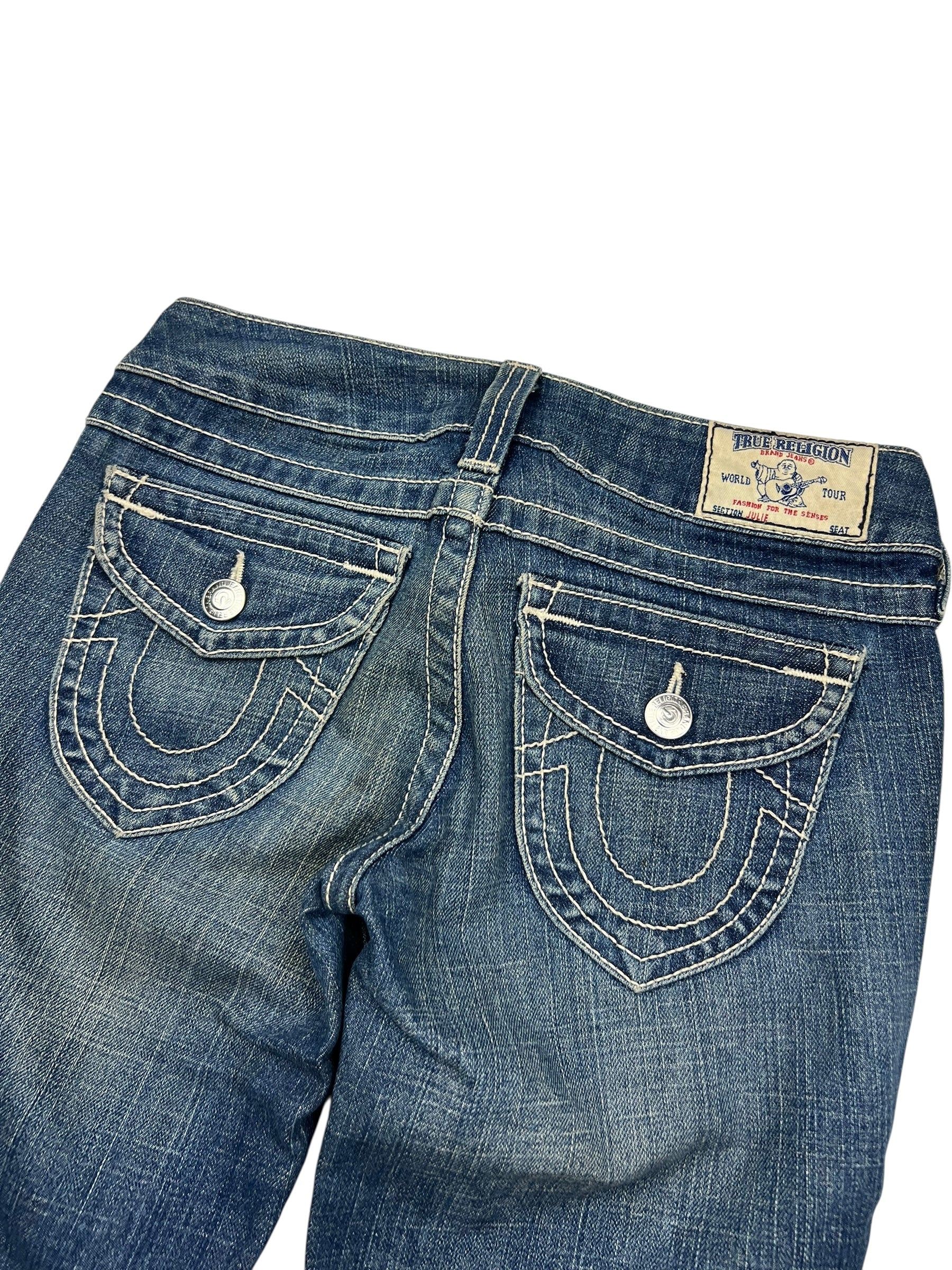 Eine Nahaufnahme der Rückseite der True Religion Skinny Jeans (Größe 25/S) von ZAZA resell aus blauem Denim mit weißen Nähten, Pattentaschen mit Knopfverschluss, einem Markenaufnäher am Bund und einem Labelgrößen-Tag in der Nähe des Größenbereichs.