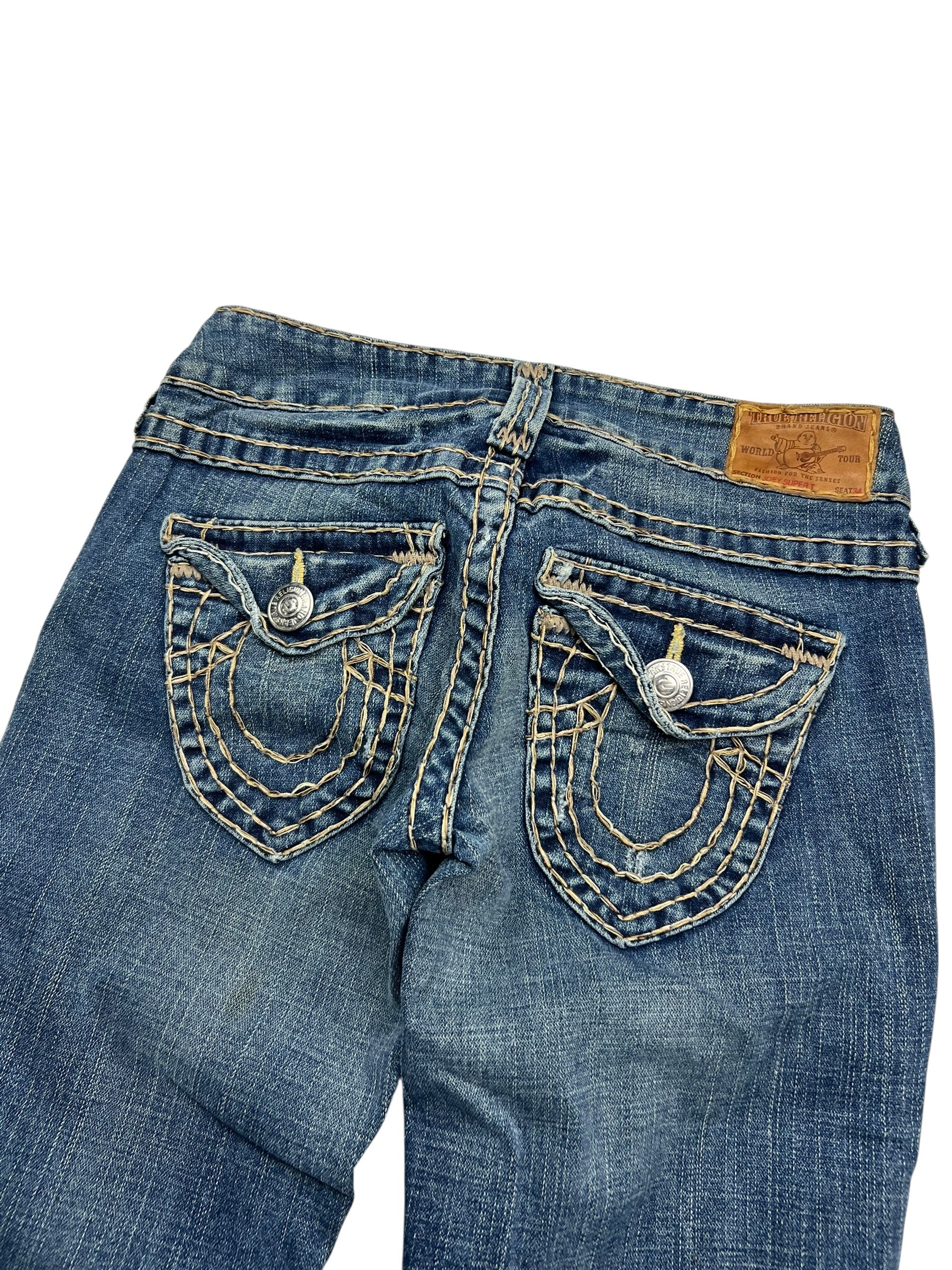Die True Religion Joey Super T - Low Rise Boot Jeans von ZAZA resell verfügt über detaillierte weiße Nähte an den Gesäßtaschen, silberne Knöpfe, einen braunen Markenaufnäher aus Leder, einen leicht ausgeblichenen Look und Labelgröße/Bundweite-Details für eine perfekte Passform. Größe: 26 (S).