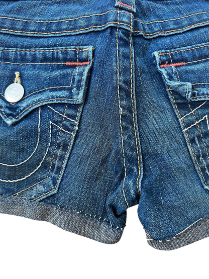 Nahaufnahme der Rückseite der True Religion Shorts | 23 (XS) von ZAZA resell aus blauem Denim, mit zwei Taschen, weißen Nähten, Metallknöpfen, roten Fadenakzenten, gerolltem Saum und einer abgenutzten Textur für einen authentischen Cowboy-Look.