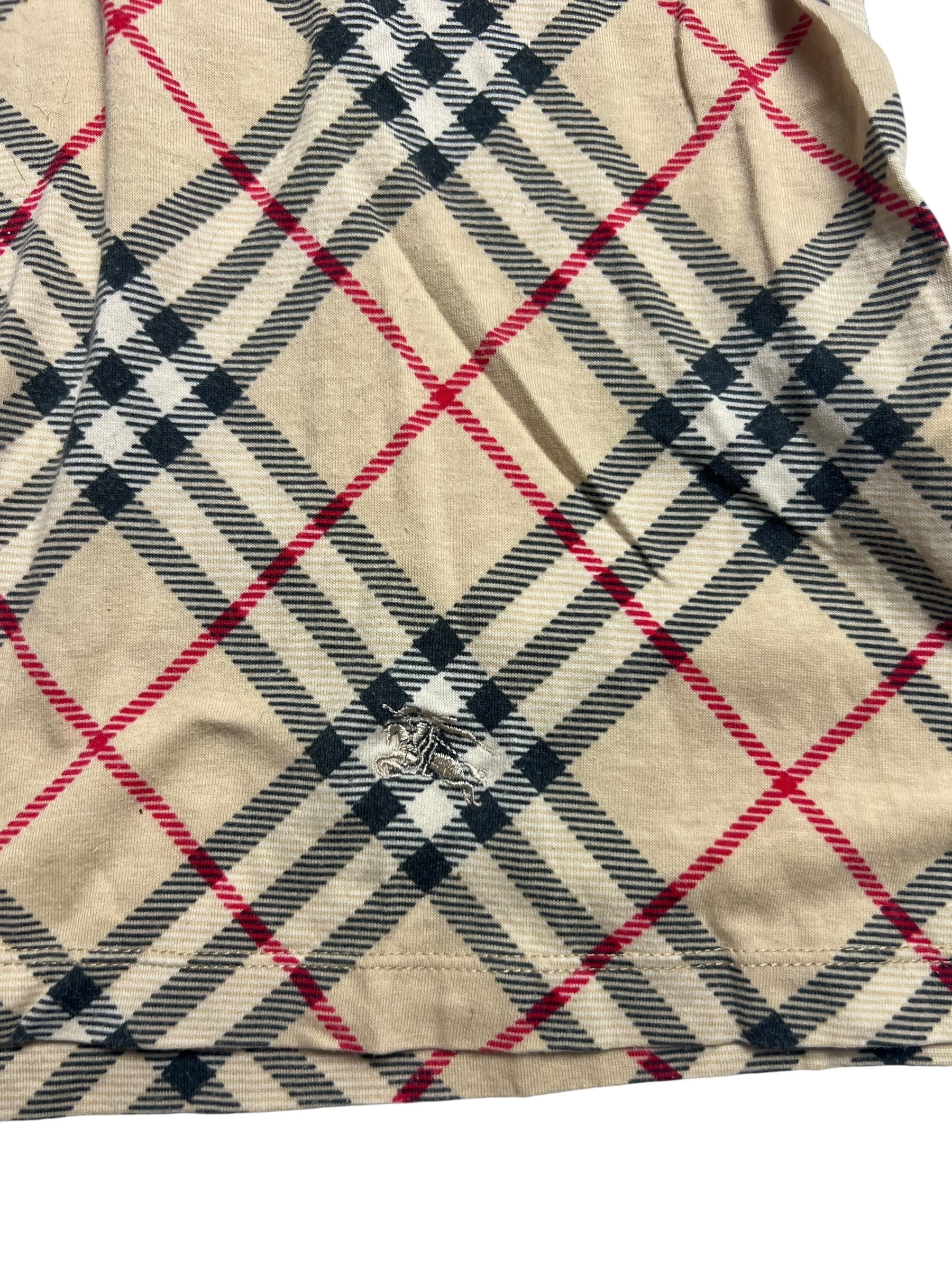 Das Burberry Polo Shirt | S von ZAZA resell ist ein beiger Stoff mit schwarzen, weißen und roten Karos. Es hat ein ausgefranstes Loch in der Nähe der Mitte, das beschädigte Fäden freilegt. Der Zustand wird mit 5/10 bewertet.