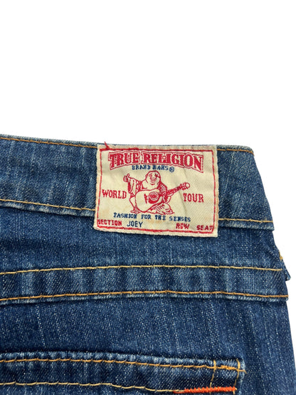 Eine Nahaufnahme der blauen Jeans True Religion Joey - Low Rise Boot von ZAZA resell, Größe 24 (S), mit einem Etikett mit einem Gitarre spielenden Buddha und Angaben wie World Tour, Section Joey, Row Seat.