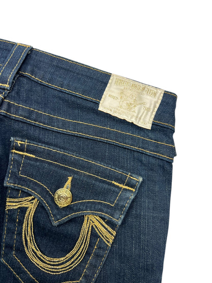 Nahaufnahme der True Religion Becky Low Rise Boot Jeans von ZAZA resell in Größe 26 (S), blauer Denim mit goldenen Nähten, Vordertasche mit Klappe und Knopf und einem weißen Bundetikett. Breite der Taille: 38,5 cm.