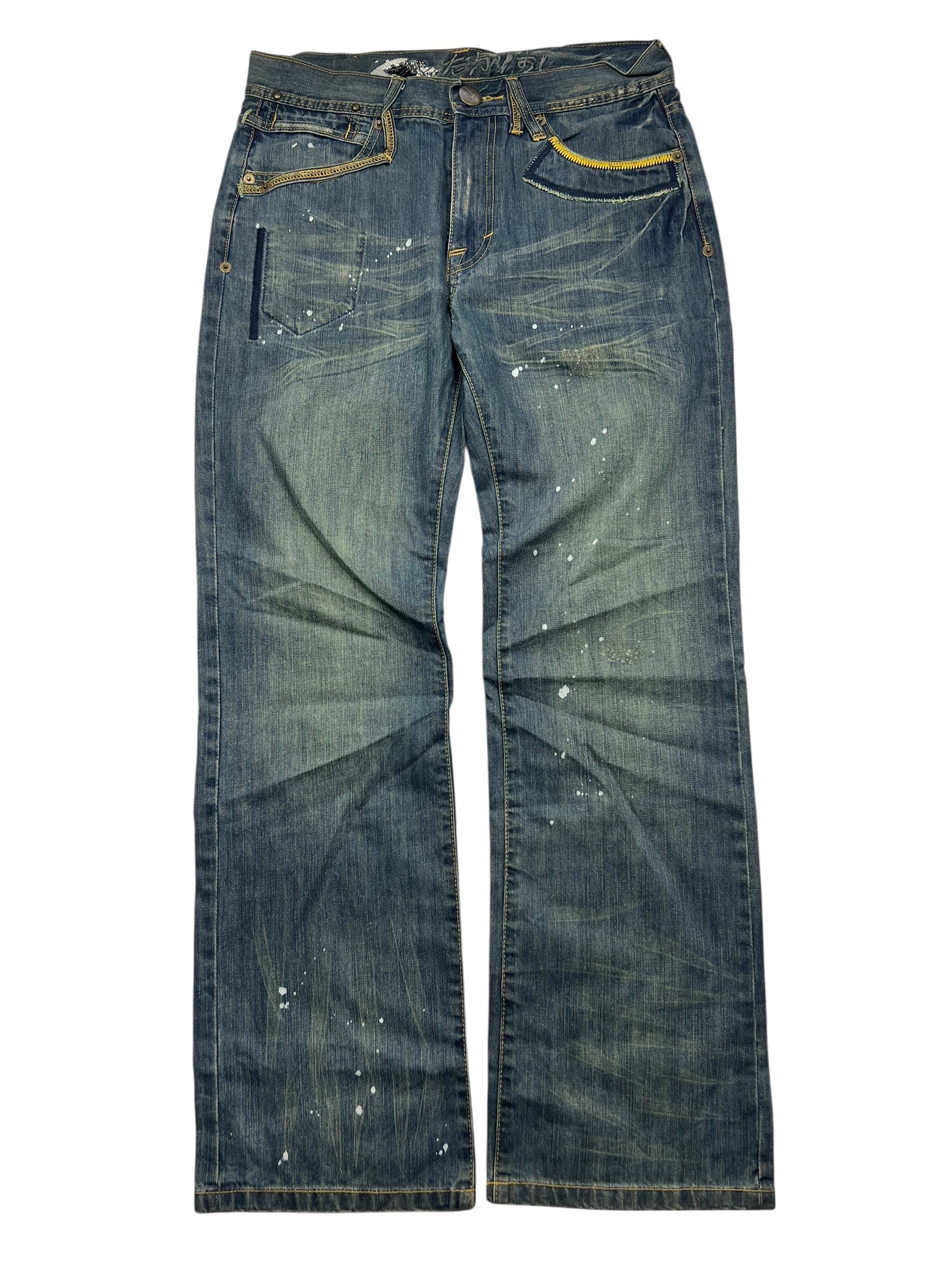 Die ZAZA resell Big Train Boot Jeans in Größe M/L hat eine blaue, verwaschene Waschung, weiße Farbkleckse und gelbe Nähte. Bundweite und Außenbeinlänge vorhanden. Jeans sind flach auf einem weißen Hintergrund gezeigt.