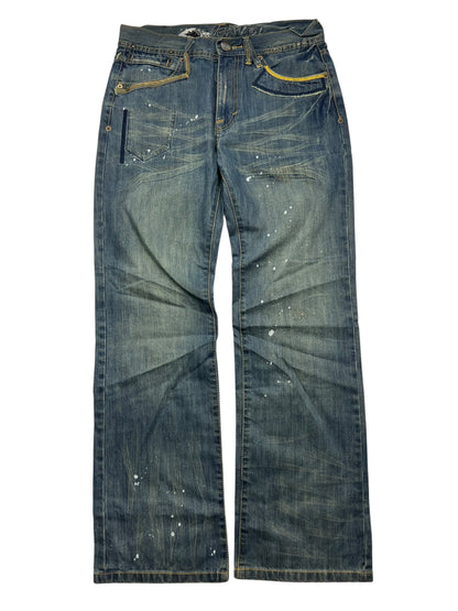 Die ZAZA resell Big Train Boot Jeans in Größe M/L hat eine blaue, verwaschene Waschung, weiße Farbkleckse und gelbe Nähte. Bundweite und Außenbeinlänge vorhanden. Jeans sind flach auf einem weißen Hintergrund gezeigt.
