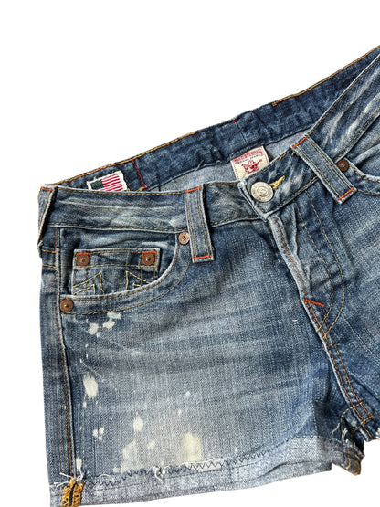 Eine Nahaufnahme der True Religion Shorts | 27 (M) mit Bundweite 39 von ZAZA resell, mit Distressed Denim, verblassten Bereichen, Farbspritzern, freiliegenden Nähten, einer Vordertasche, Gürtelschlaufen und einem sichtbaren Knopfverschluss.