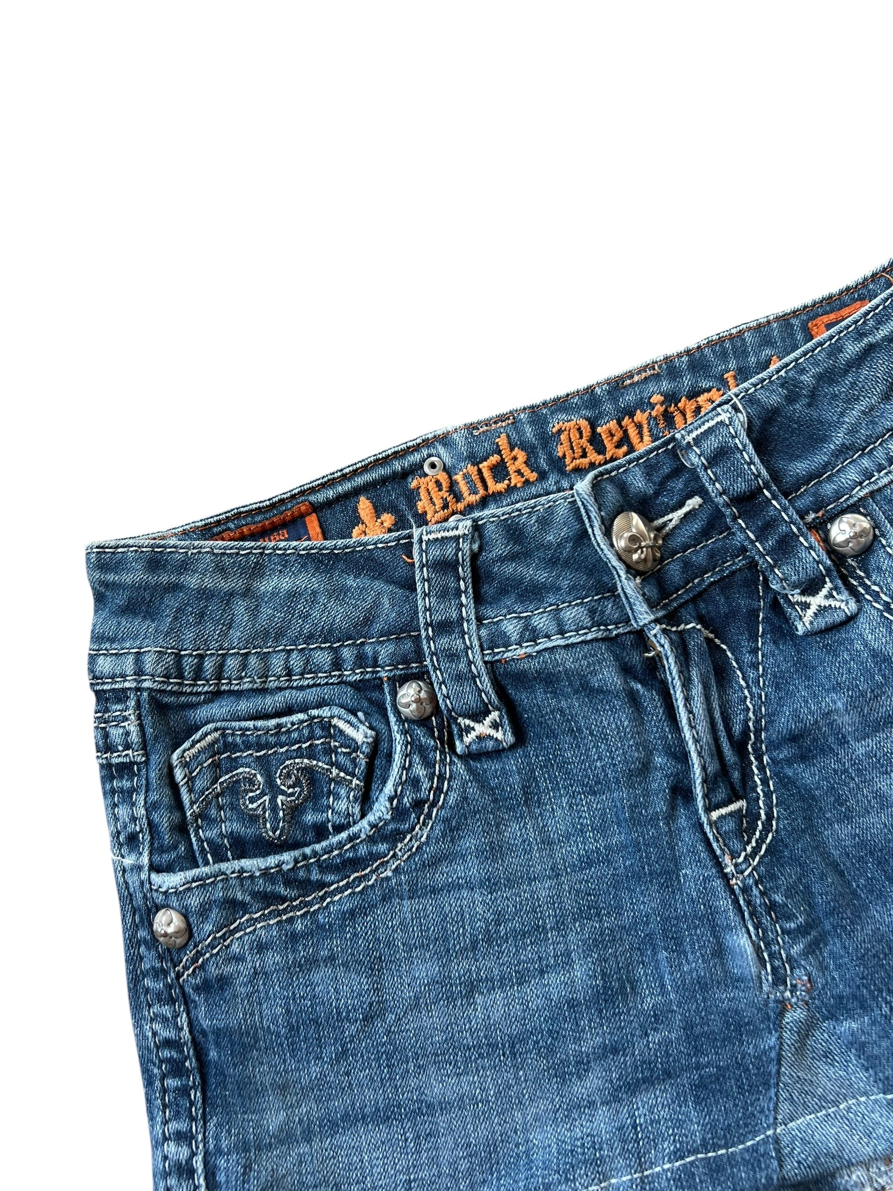 Nahaufnahme des Rock Revival Rocks in Größe 25 (XS) von ZAZA resell. Hervorzuheben sind der Bund, der Knopf, die Gürtelschlaufen und die Vordertasche. Der Innenbund zeigt das orangefarbene Rock Revival-Branding und ein Fleur-de-Lis-Taschendesign.