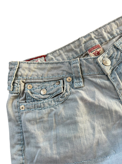 Nahaufnahme der True Religion Shorts von ZAZA resell aus hellblauem Denim, mit sichtbaren Nähten, Metallnieten an der Vordertasche, einer kleinen Münztasche, Gürtelschlaufen und einem teilweise sichtbaren Markenetikett im Bund. Maße in Zentimetern. Größe: 30 (M).