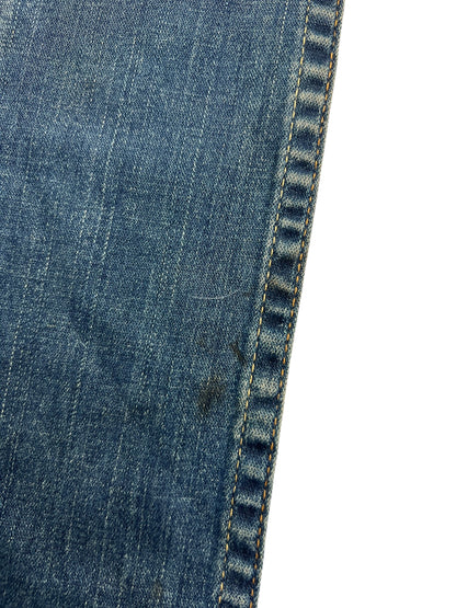 Nahaufnahme von blauem Denim-Stoff mit gelben Nähten und einem kleinen Fleck in der Nähe der Naht. Die True Religion Billy - Low Rise Straight | 24 (S) von ZAZA resell vereint ideale Passform und Qualität für Detailverliebte.