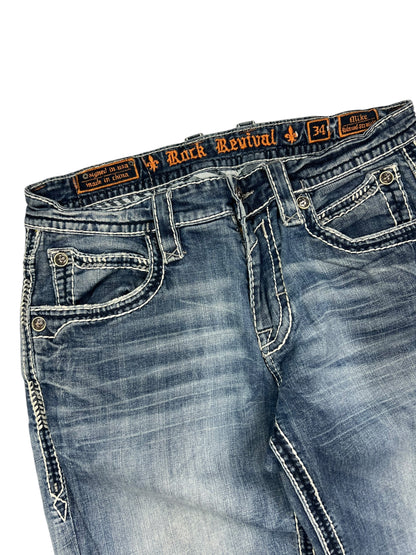 Eine Nahaufnahme der blauen ZAZA resell Rock Revival Relaxed Straight/Baggy Jeans in Größe 34 (M) mit weißen Kontrastnähten, dekorativen Vordertaschen und einem Bundweite-Label am Bund.