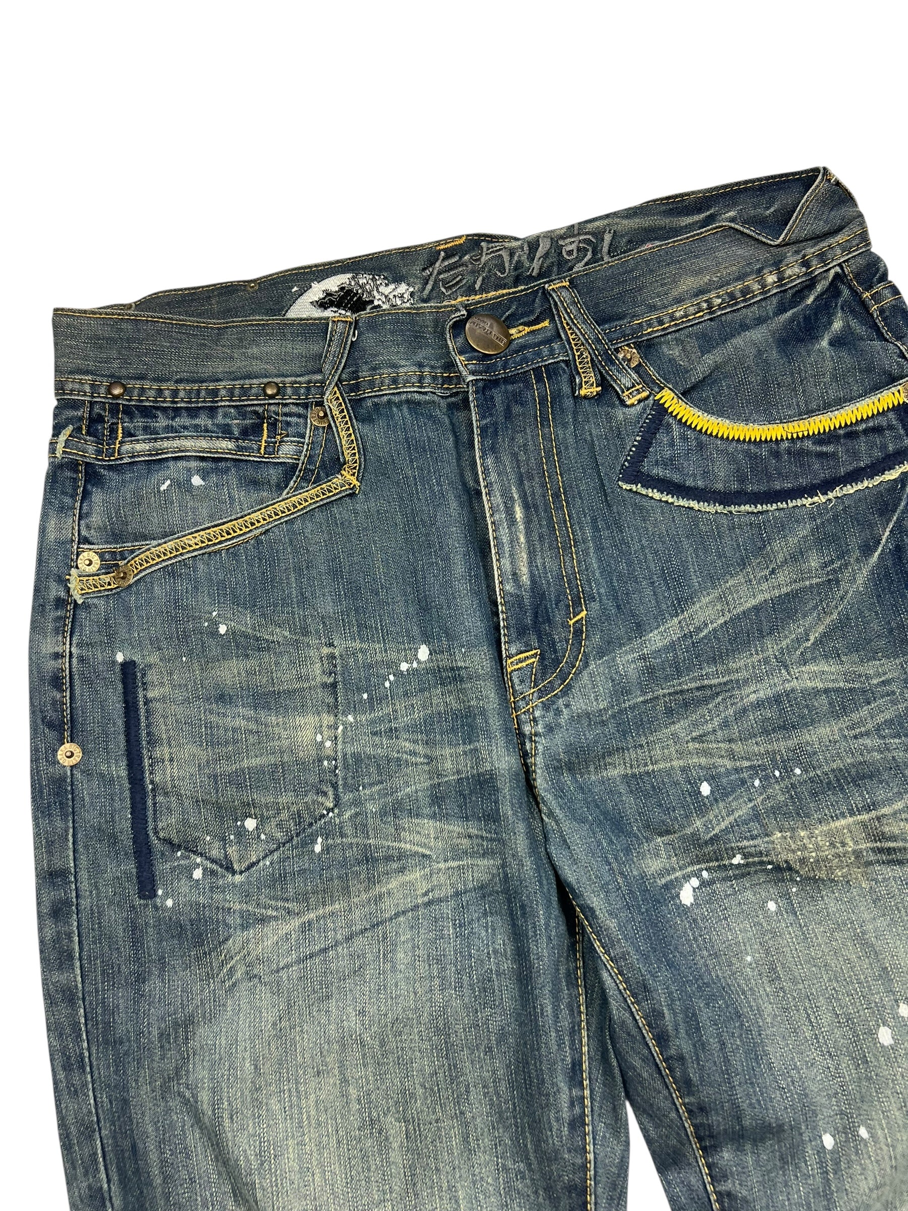 Die Big Train Boot Jeans von ZAZA resell in M/L hat blauen Distressed-Denim, Farbspritzer, einen gelben Reißverschluss an einer Tasche, sichtbares Fading und Whiskering und eine Außenbeinlänge für eine bequeme Passform.