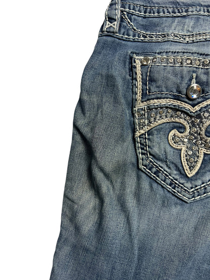 Eine Nahaufnahme der Rock Revival Mid Rise Boot | 32 (XL) Jeans von ZAZA resell zeigt einen verblichenen, abgenutzten Look und ein Oberteil mit einer bestickten, strassbesetzten Gesäßtasche. Bundweite 46 und Außenbeinlänge 110 sorgen für eine einzigartige Passform.