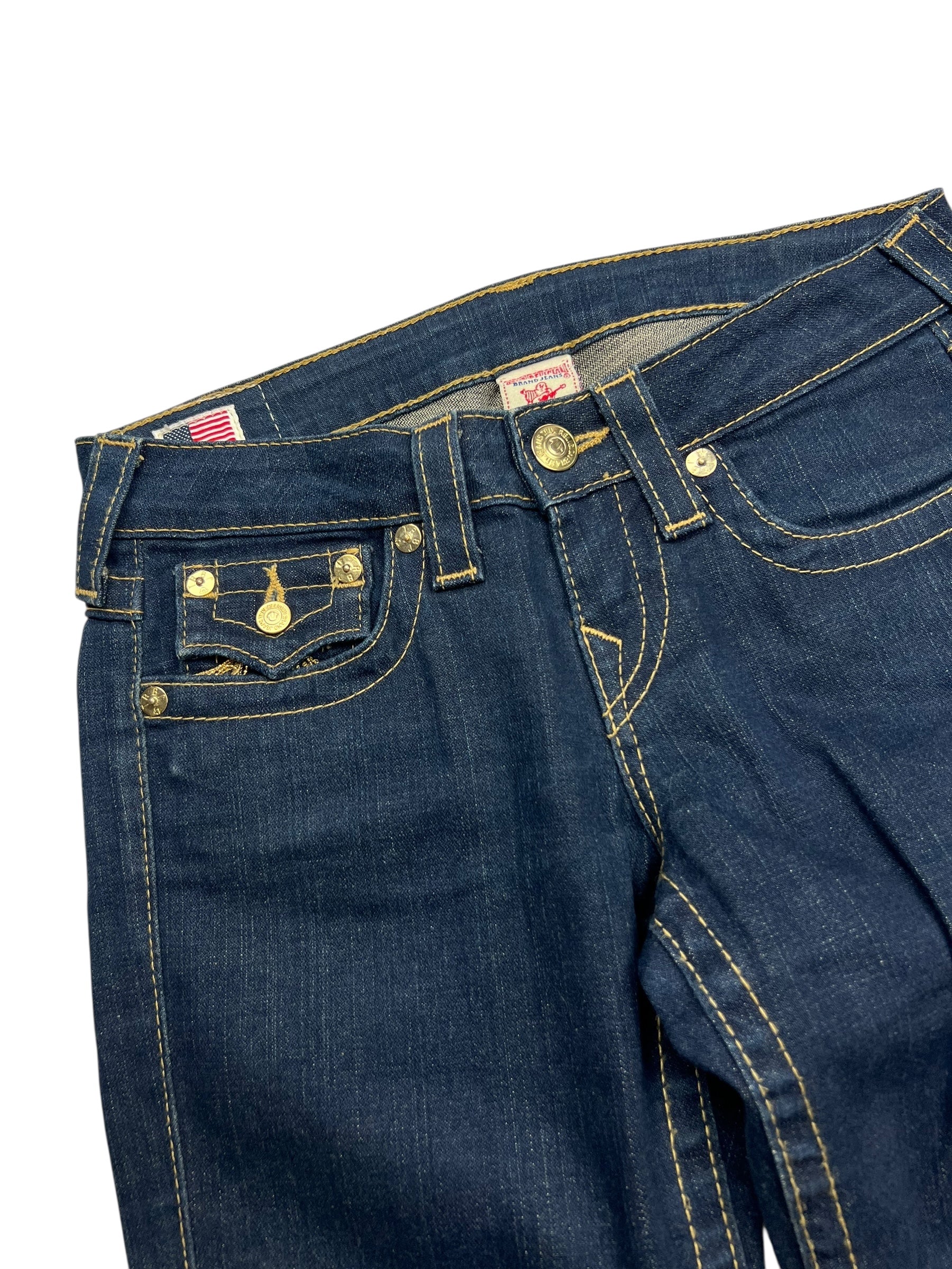 Eine Nahaufnahme der True Religion Becky - Low Rise Boot Jeans in Größe 26 (S) von ZAZA resell, mit seltenem blauen Denim, goldenen Nähten, Bund, Vordertaschen, Knöpfen und Gürtelschlaufen auf weißem Hintergrund.