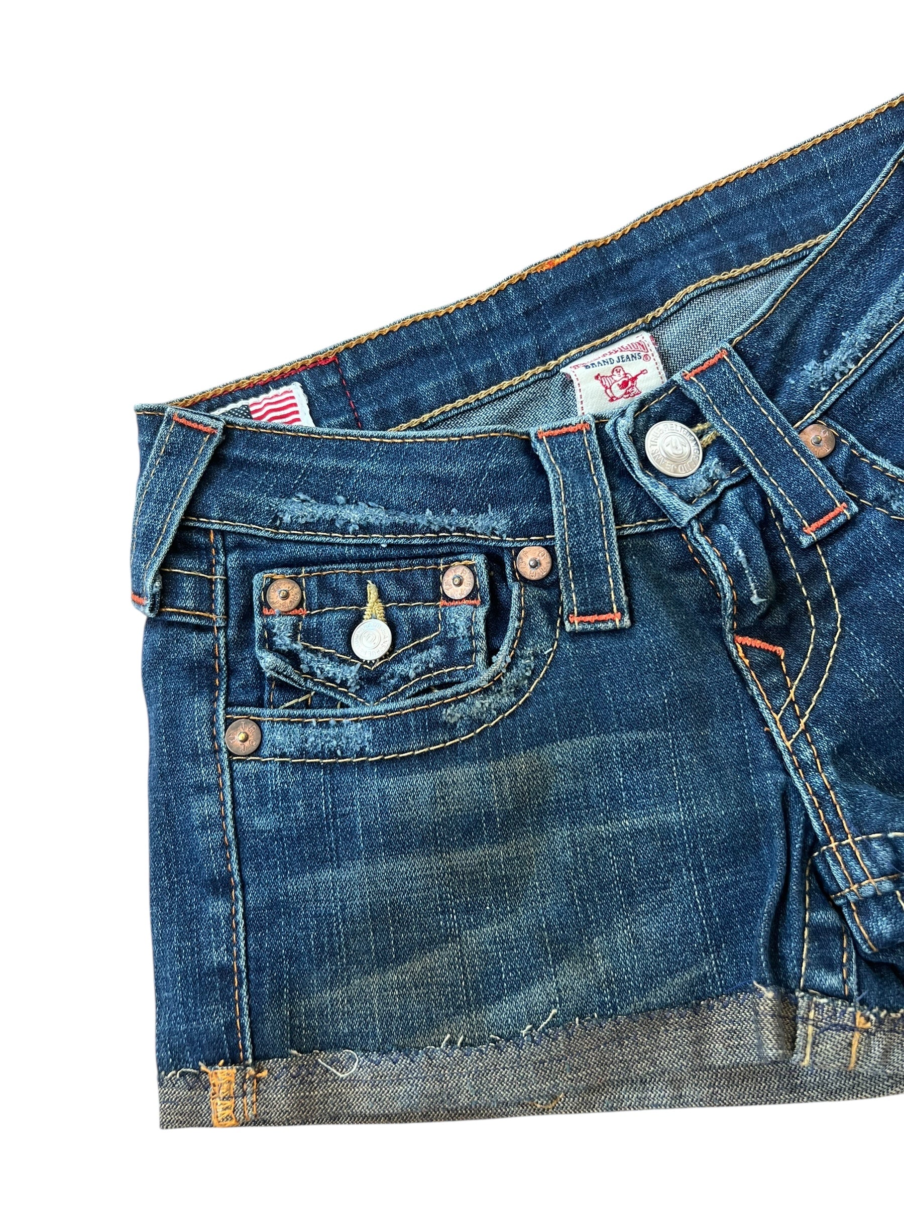 Die True Religion Shorts | 23 (XS) von ZAZA resell haben einen ausgefransten, abgeschnittenen Saum mit Fronttasche, Gürtelschlaufen, Kupfernieten und detaillierte Nähte - alles auf einem knackigen weißen Hintergrund für den klassischen Cowboy-Look.