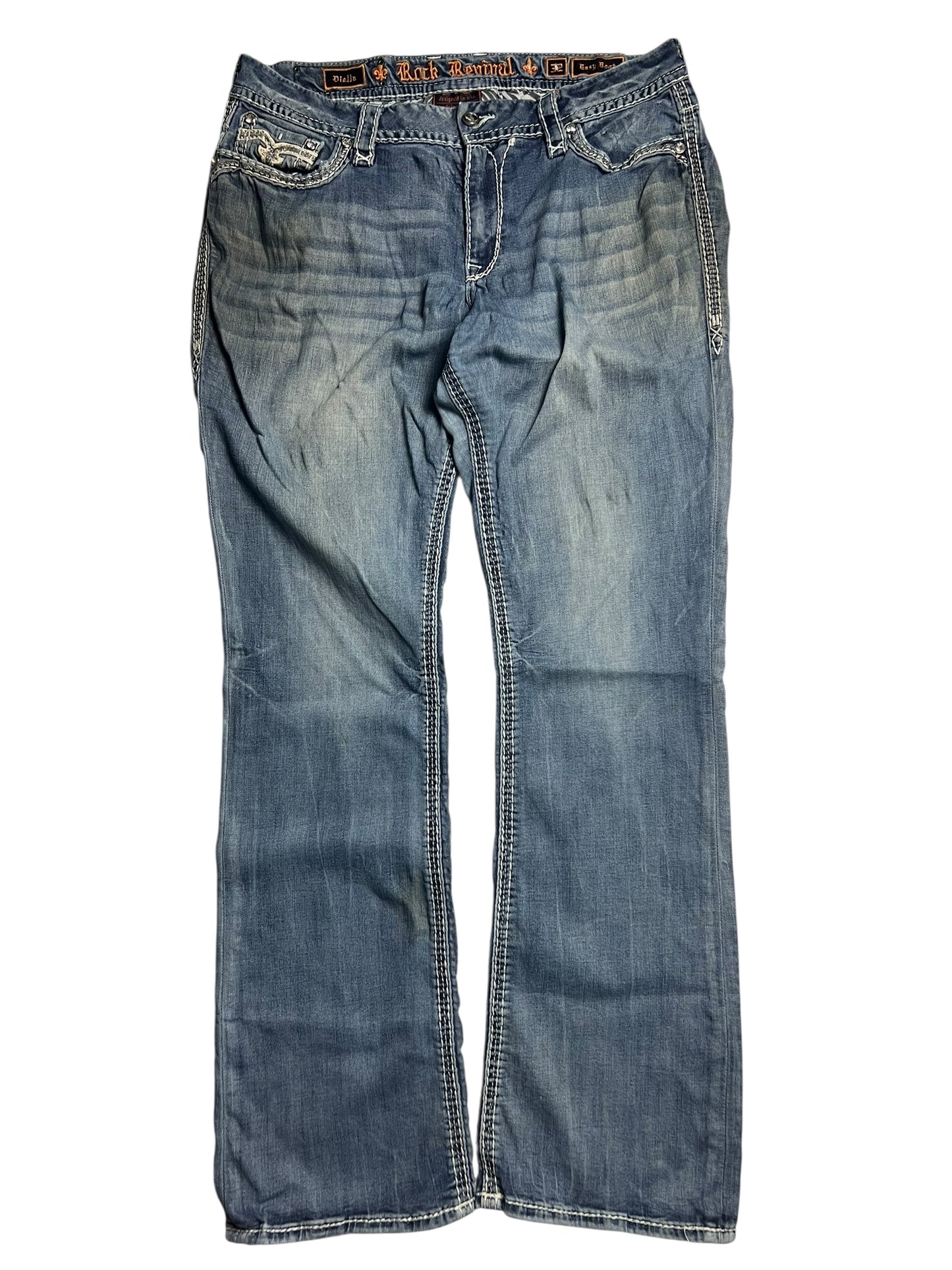 Die Rock Revival Mid Rise Boot-Jeans von ZAZA resell (Größe 32 XL, Bundweite 46) hat einen verblichenen blauen Denim, weiße Nähte, Taschen auf der Vorderseite und ein sichtbares Logo-Etikett auf dem Innenbund, das flach auf weißem Grund abgebildet ist.