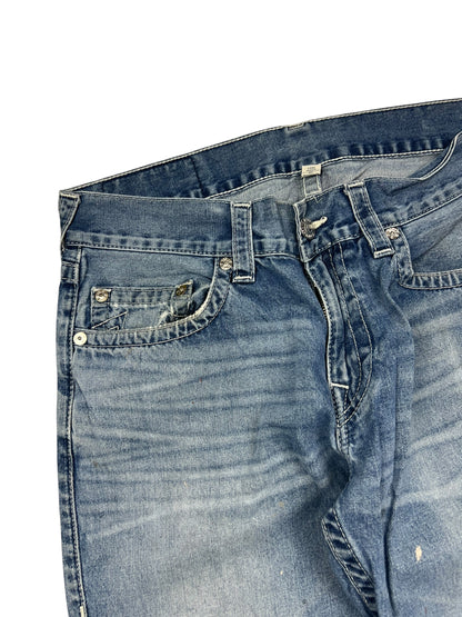 Eine Nahaufnahme der True Religion Straight | 34 (L) Blue Denim Jeans von ZAZA resell zeigt abgenutztes, verblasstes Gewebe, sichtbare Taschen, Gürtelschlaufen, einen Metallknopf und die Etikettengröße in der Nähe des Bundes auf weißem Hintergrund.