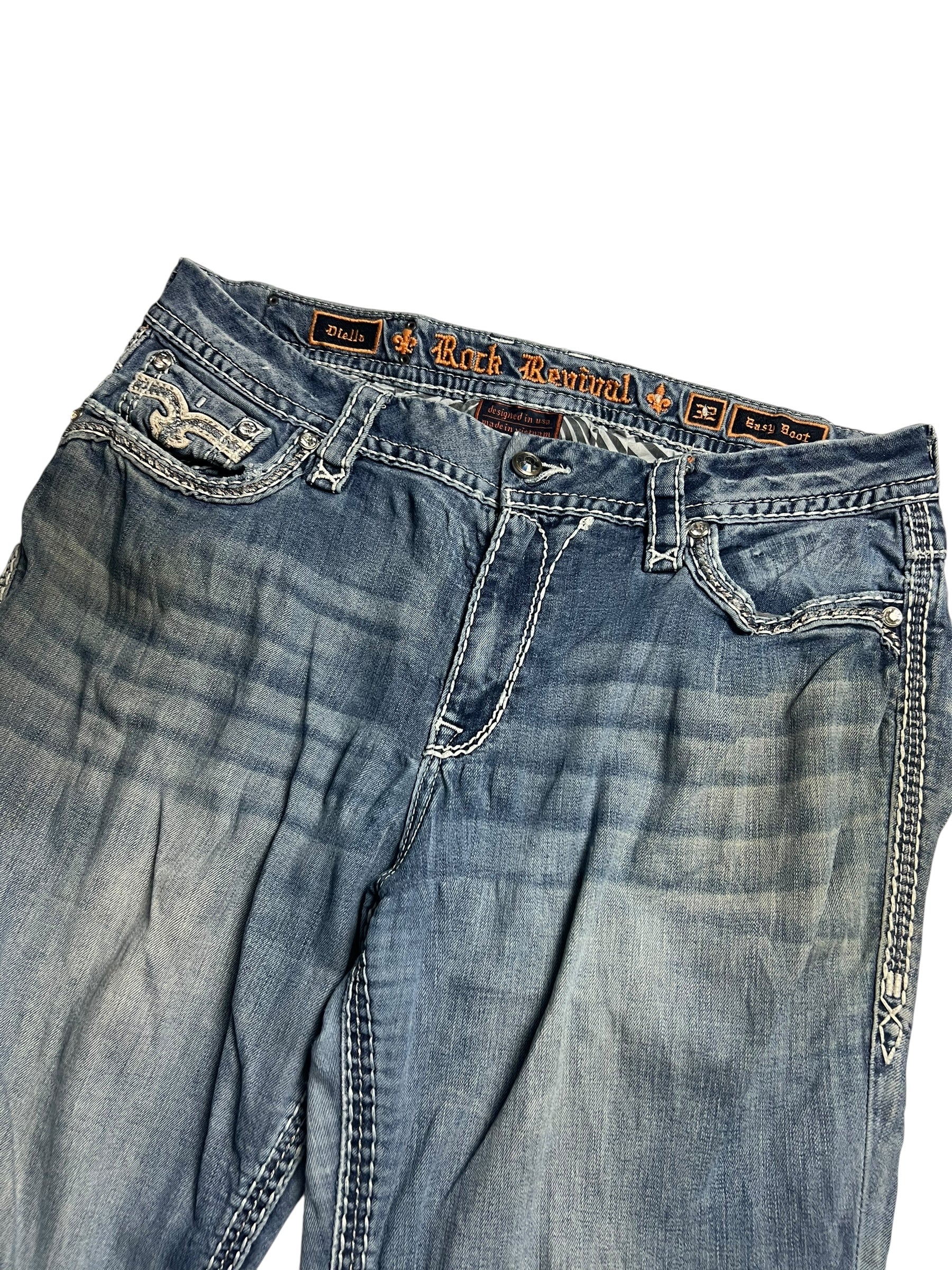 Ein Paar Rock Revival Mid Rise Boot Jeans von ZAZA resell, Größe 32 (XL), in blau mit weißen Nähten, dekorative Gesäßtaschen, abgenutzte Oberschenkel, Außenbeinlänge 110 cm, Bundweite 46 cm, abgebildet auf einem weißen Hintergrund.